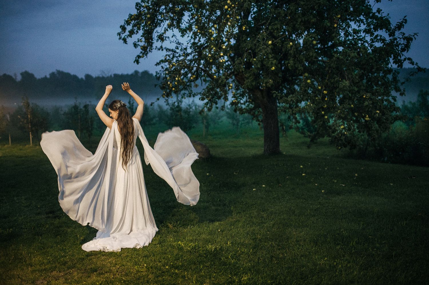 A white wedding dress flows in the breeze against a dusky blue sky during an outdoor photo session.