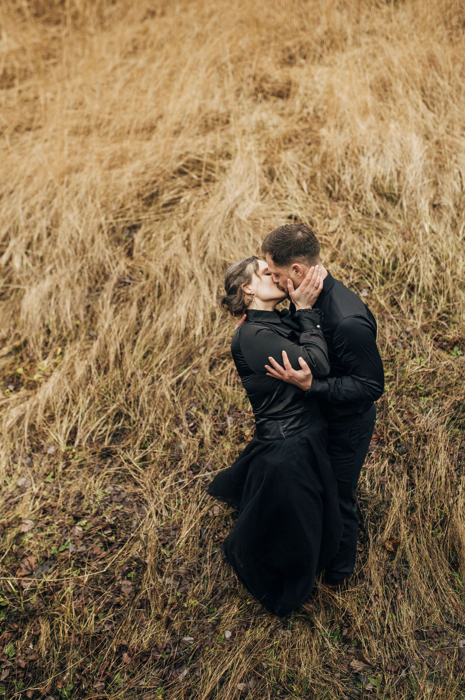 Couple dressed in black share passionate embrace in golden field.