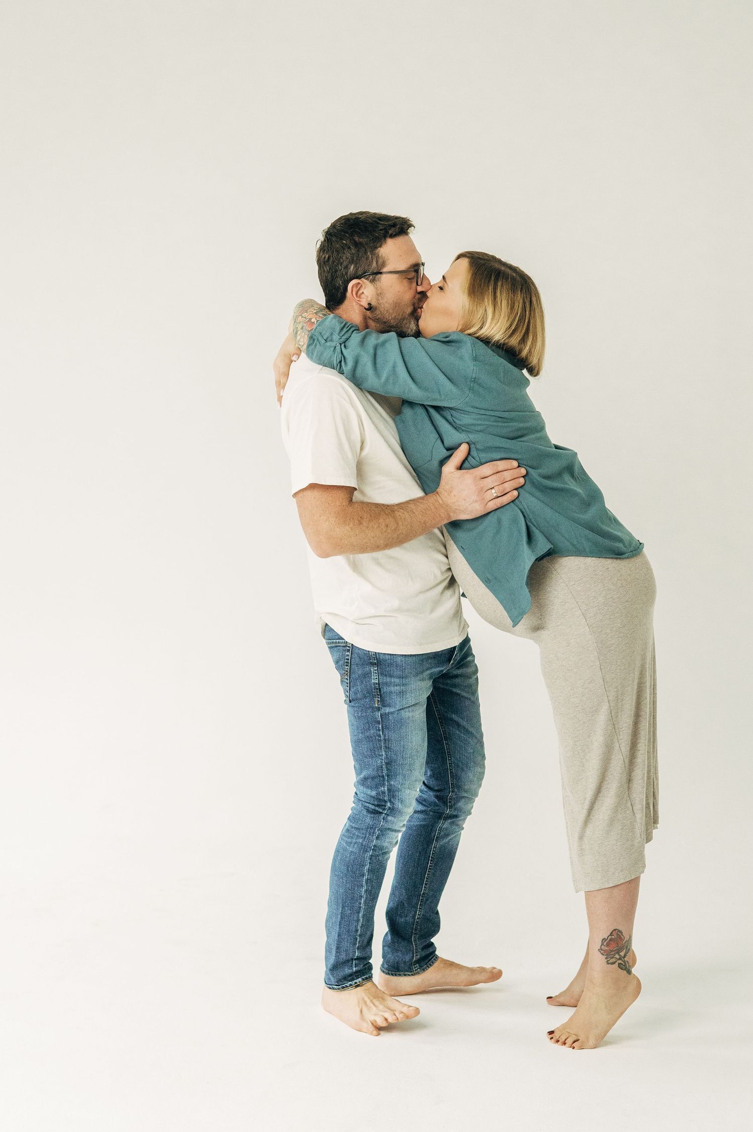 Couple shares intimate kiss while embracing during casual maternity photoshoot.