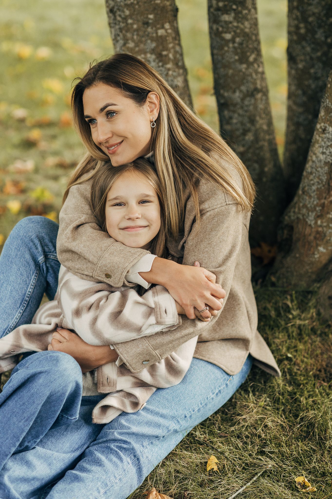 Cozy autumn moments between family members sitting under trees in casual sweaters and jeans.