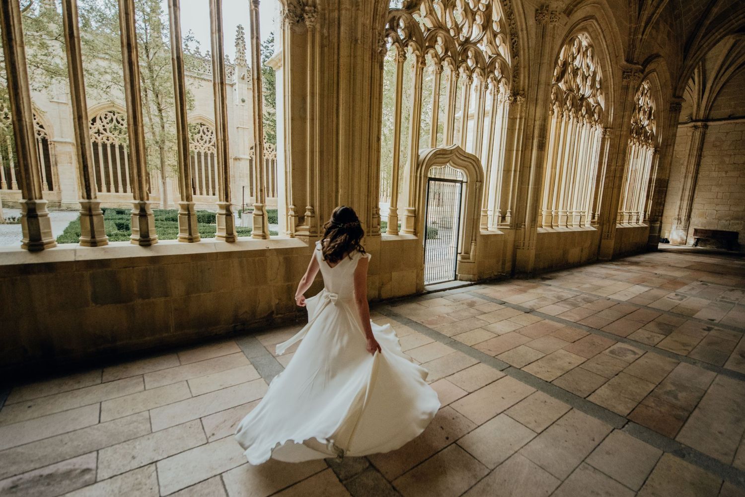 Elegant stone corridor with natural light streaming through arched windows during a bridal photoshoot.