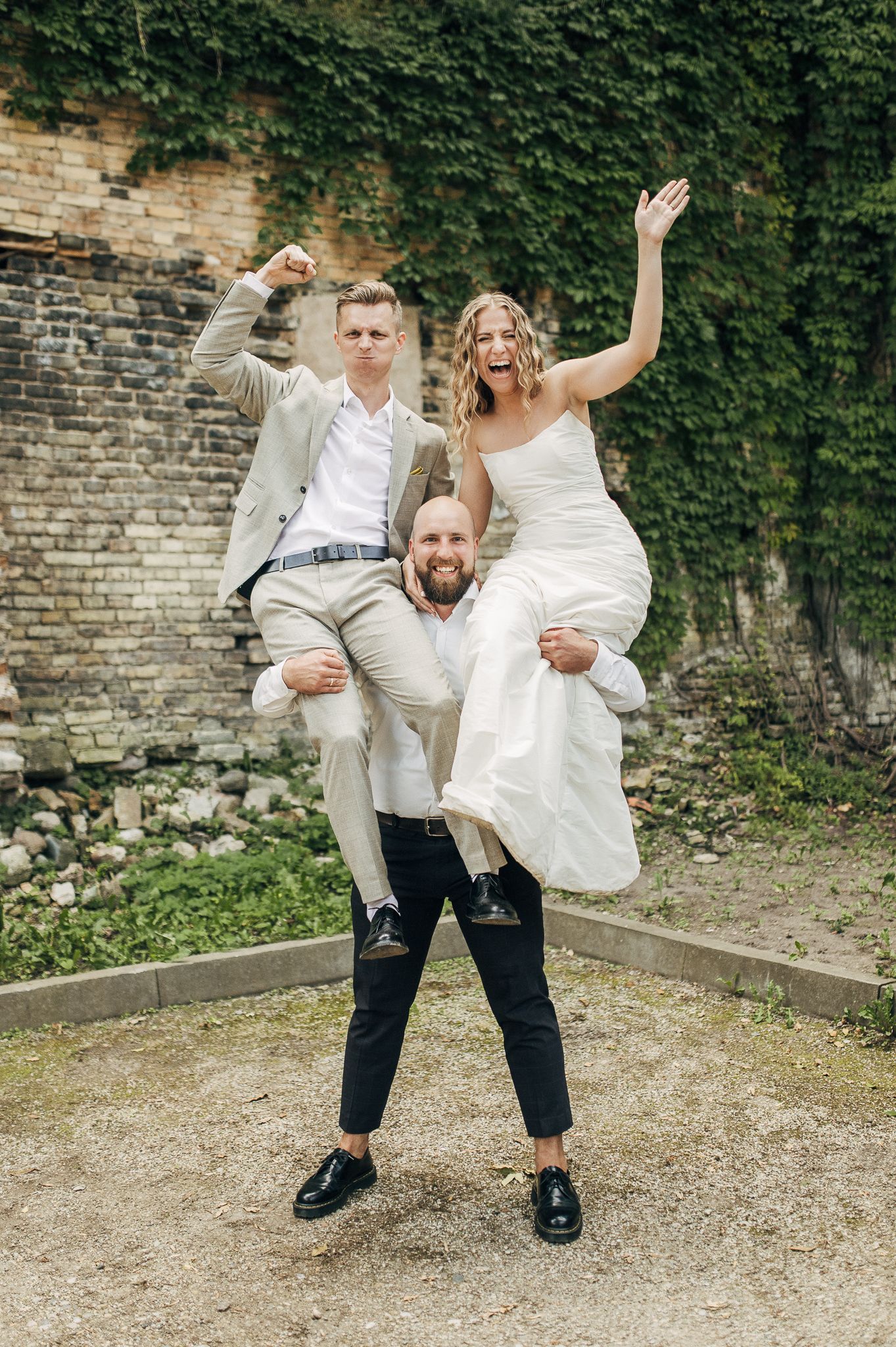 Playful wedding couple and guests posing with energetic movements against an ivy wall.