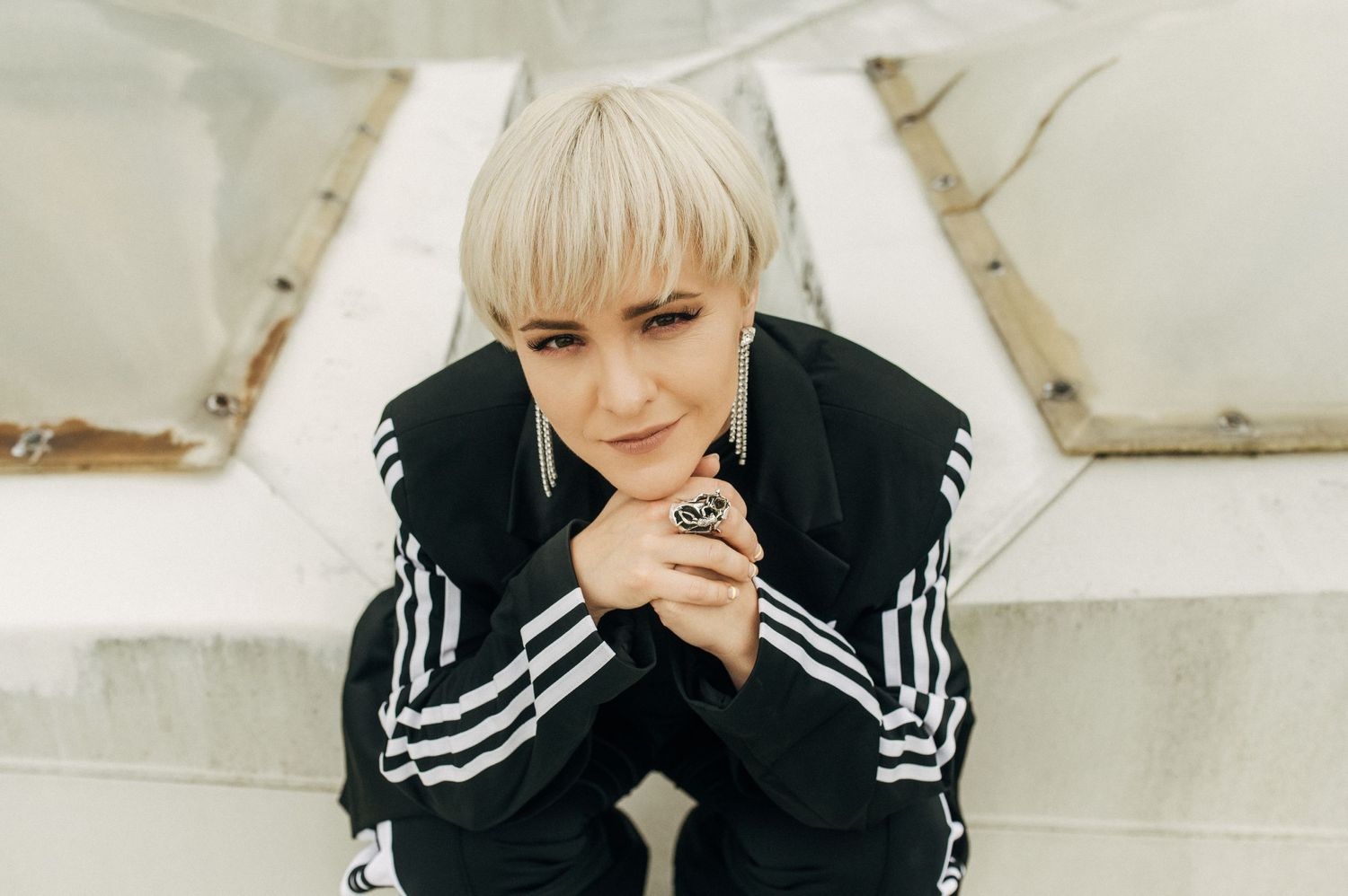 Person in striped Adidas jacket sitting with thoughtful expression against white background.