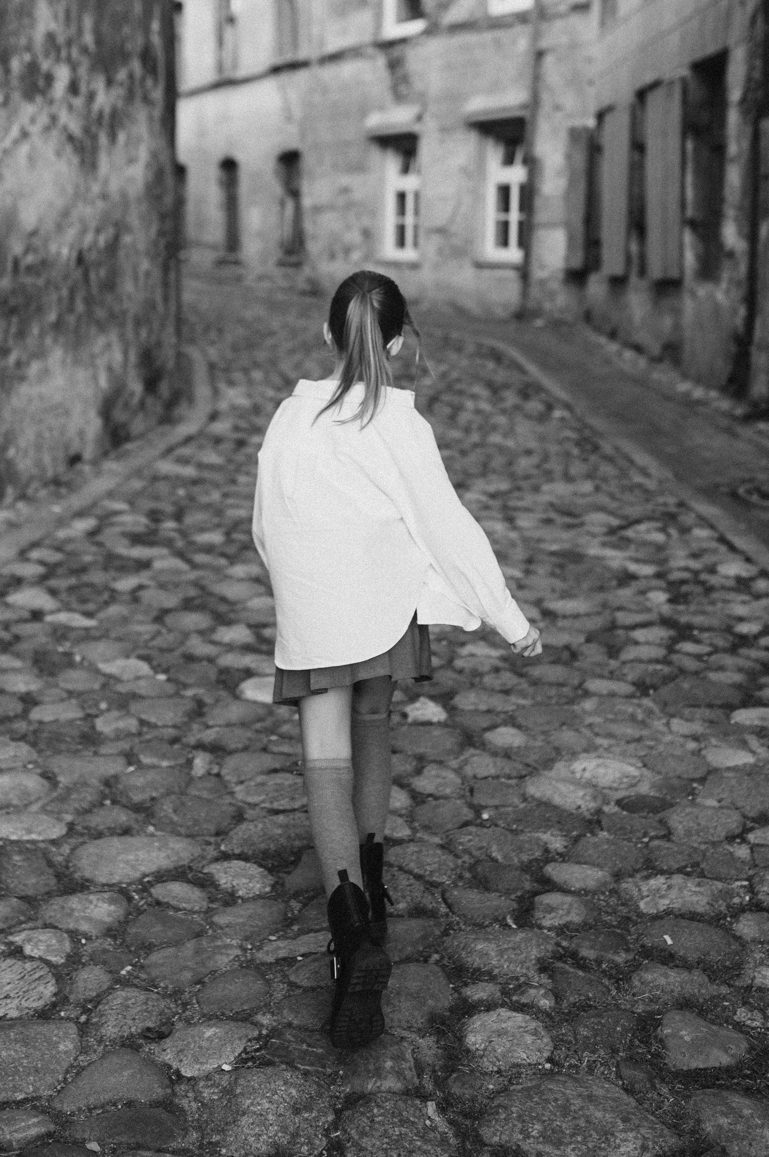 Figure in white walking on historic cobblestone street.