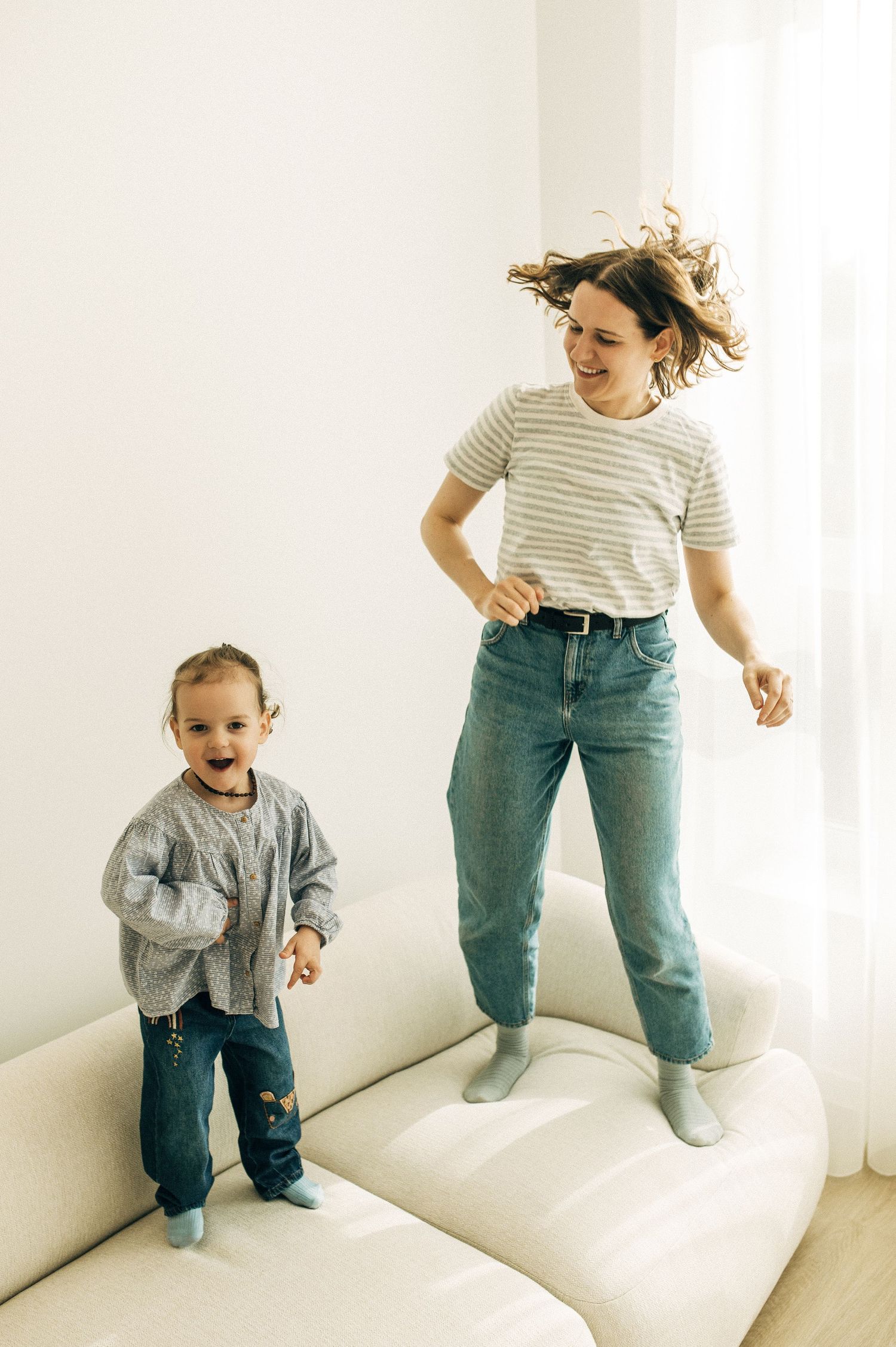 Parent and child jumping together on white couch in playful moment.