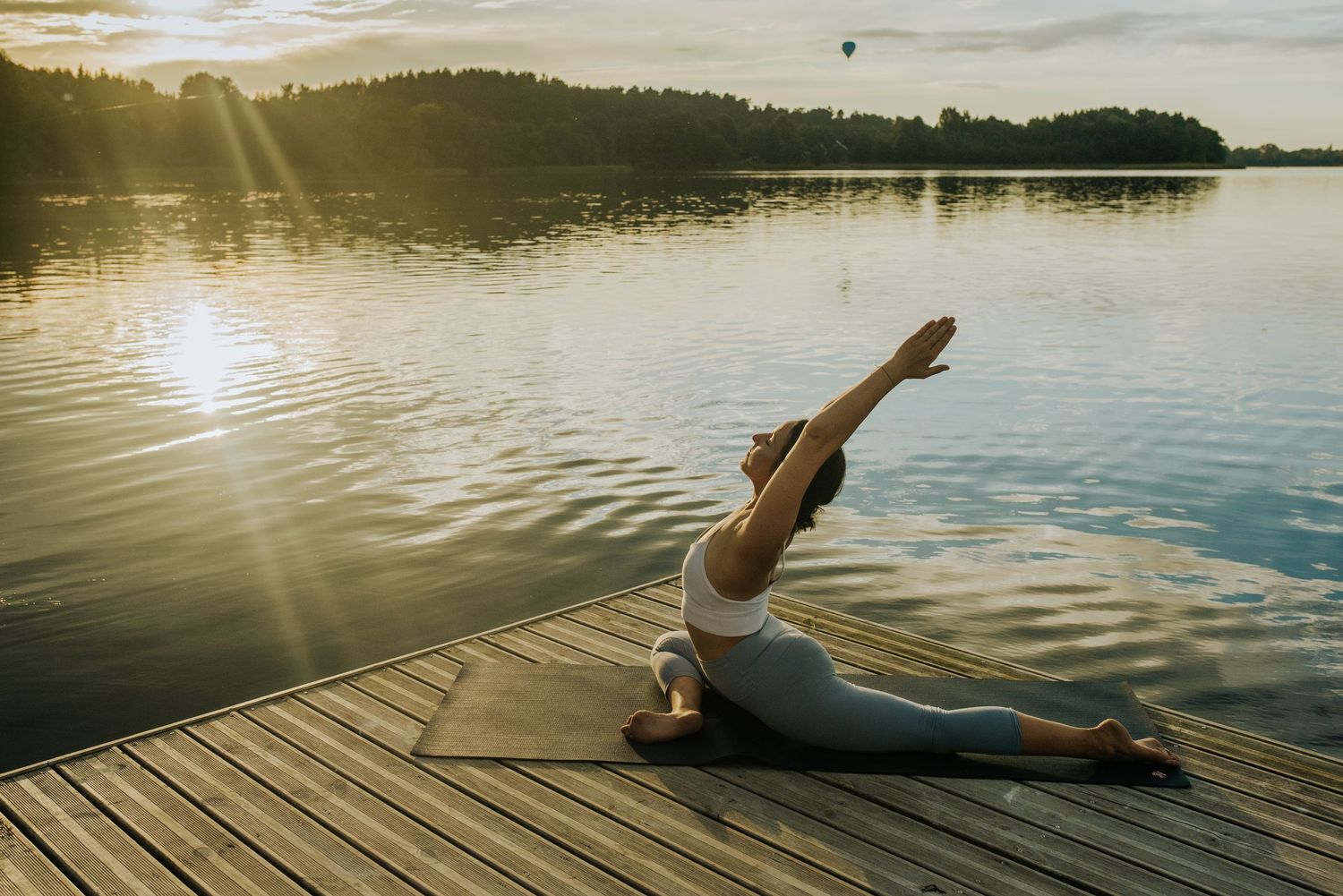 Person performs graceful movements on wooden dock with sunset lake view.