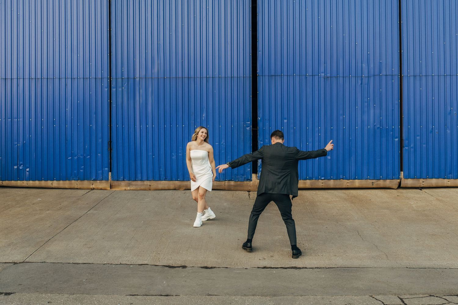 Wedding couple poses creatively against bright blue industrial wall backdrop.