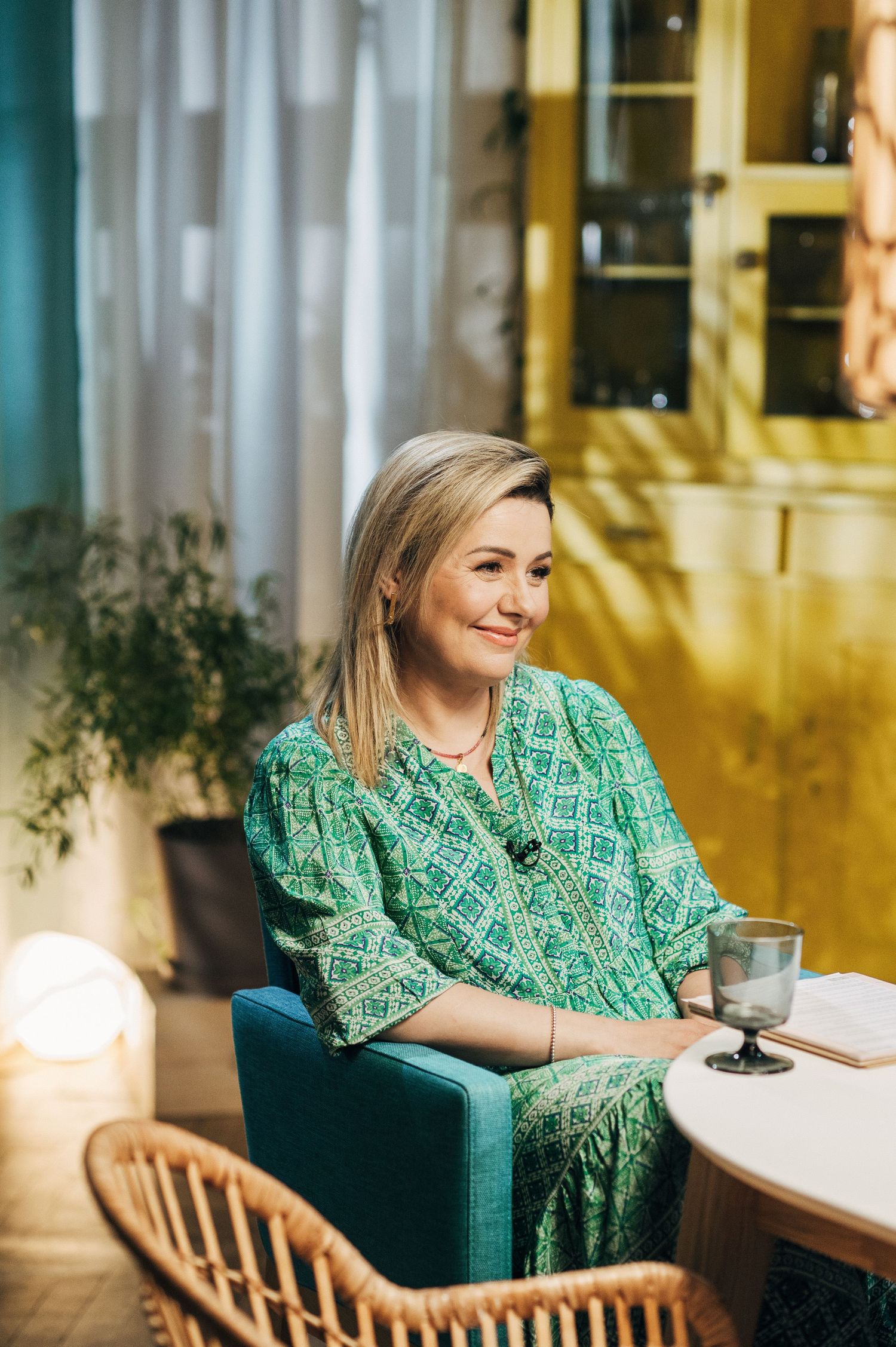 Person in green patterned dress sitting at a cafe table in warm sunlit setting.