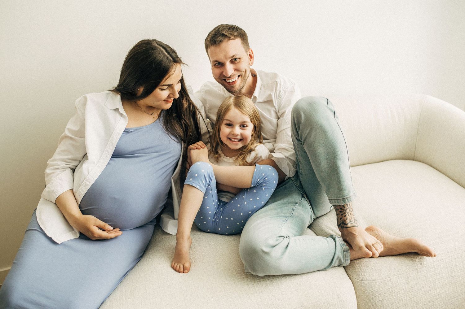 Family moment captured on white couch in light-filled room.