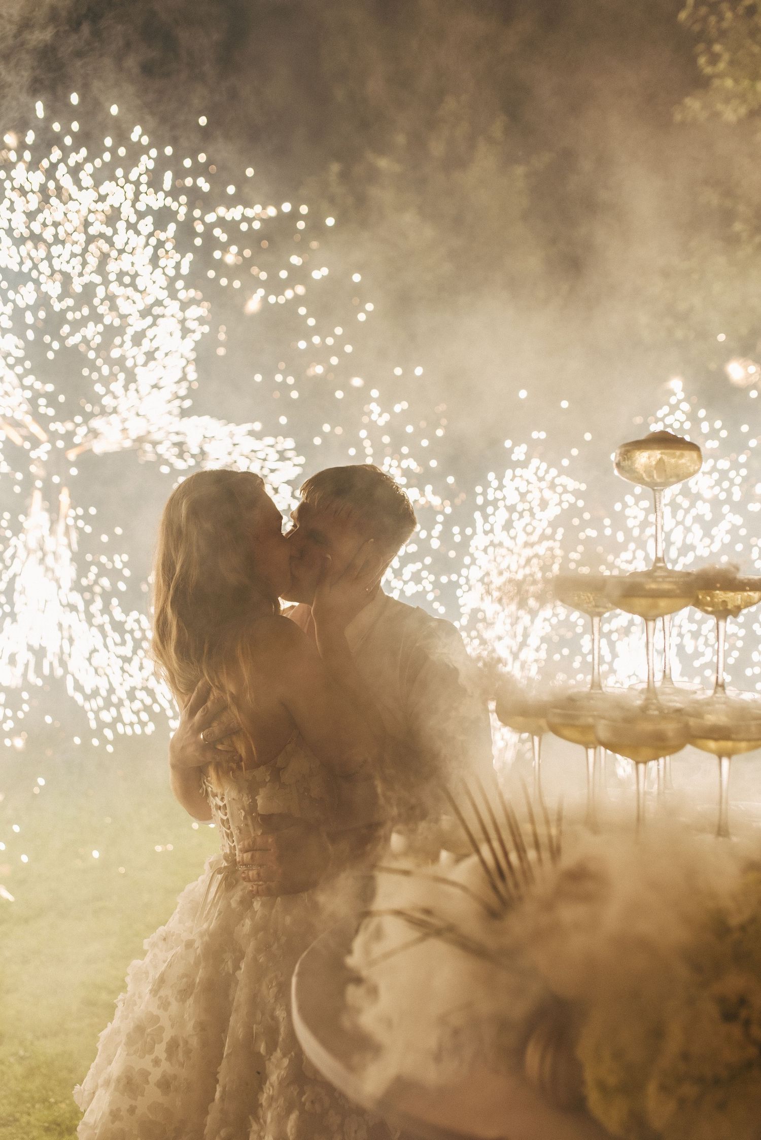 Newlyweds share a romantic moment as sparklers create a magical backdrop of light and smoke in the evening.