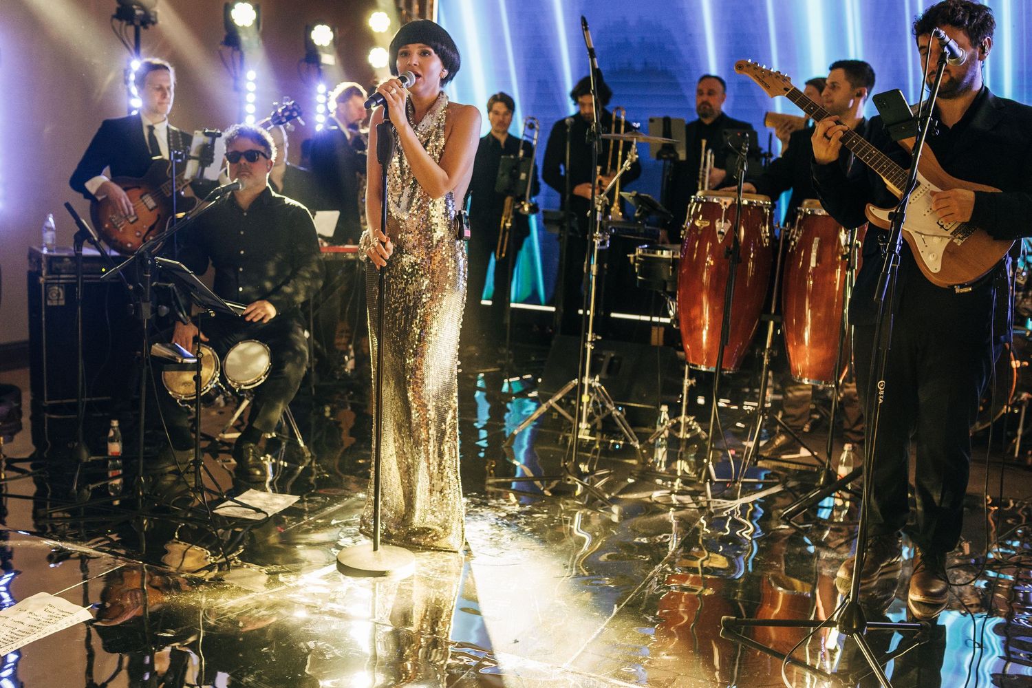 Musicians perform on stage with dramatic blue lighting and fog effects during a live concert performance.