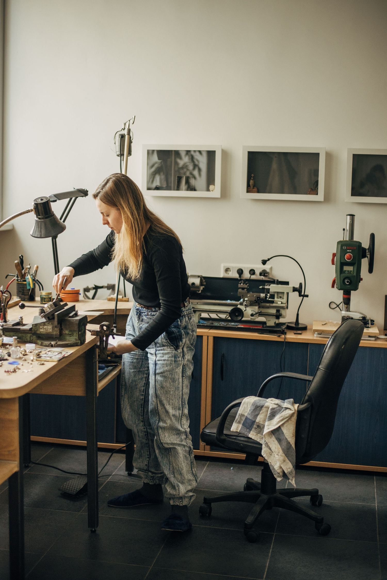 Artist working at a jewelry bench with tools and equipment in a professional studio space.