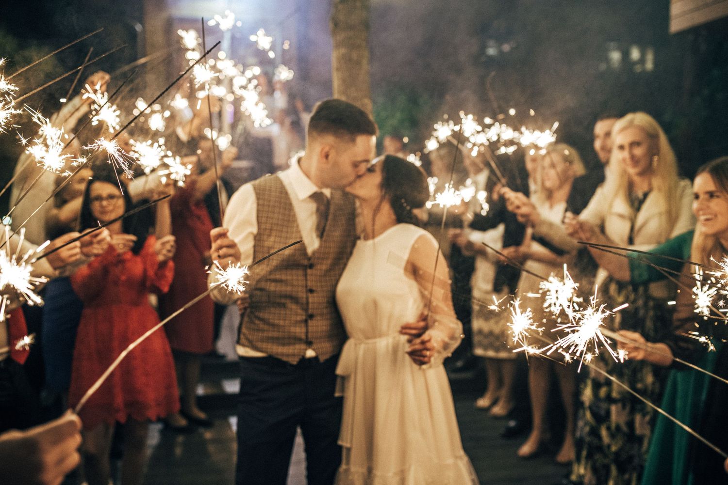 Wedding celebration with sparklers creating a magical tunnel of light at night.