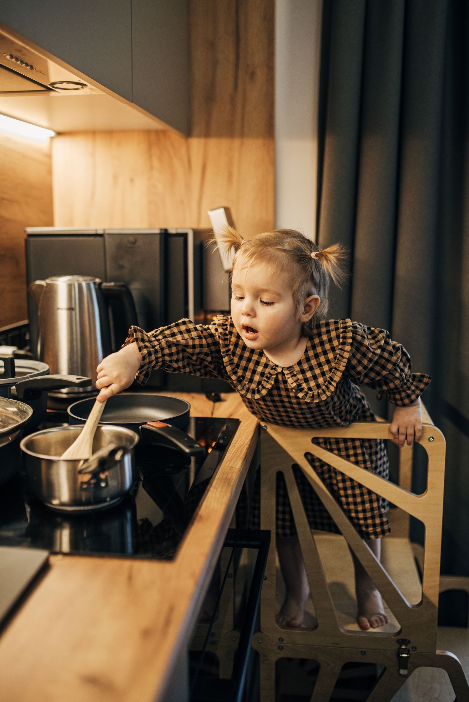 Toddler in plaid shirt reaching for pots and pans while leaning on kitchen chair in series of playful movements.