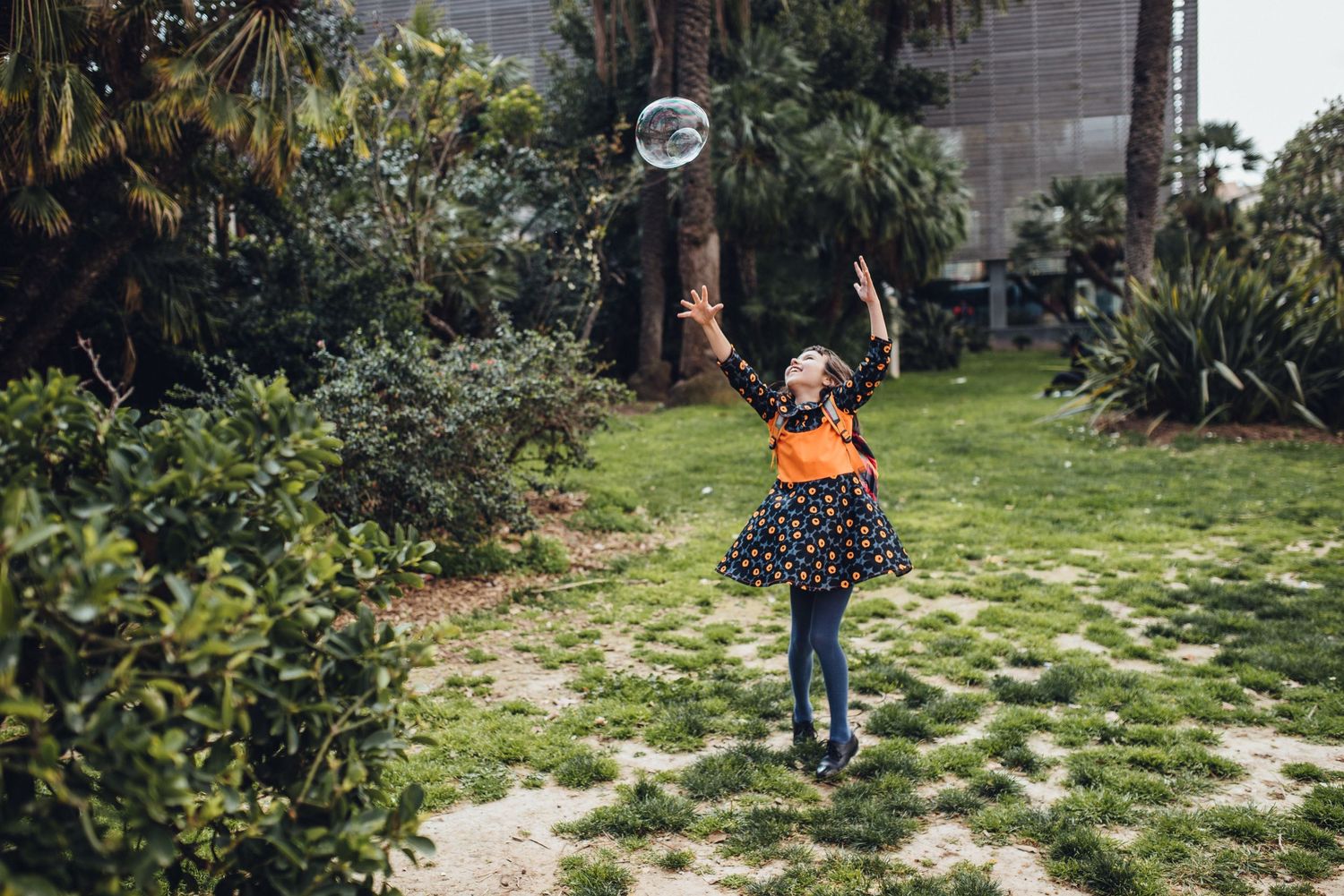 Children dance and play outdoors in a lush garden setting with natural greenery and stone pathways.