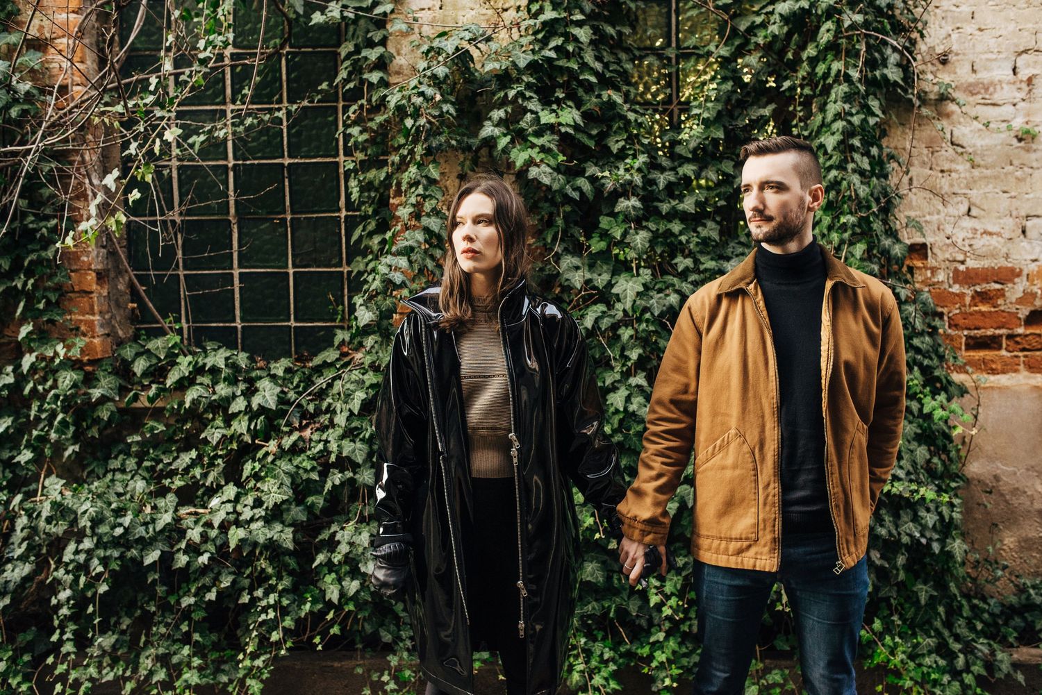A couple walks together through a lush garden setting with brick walls and climbing ivy.