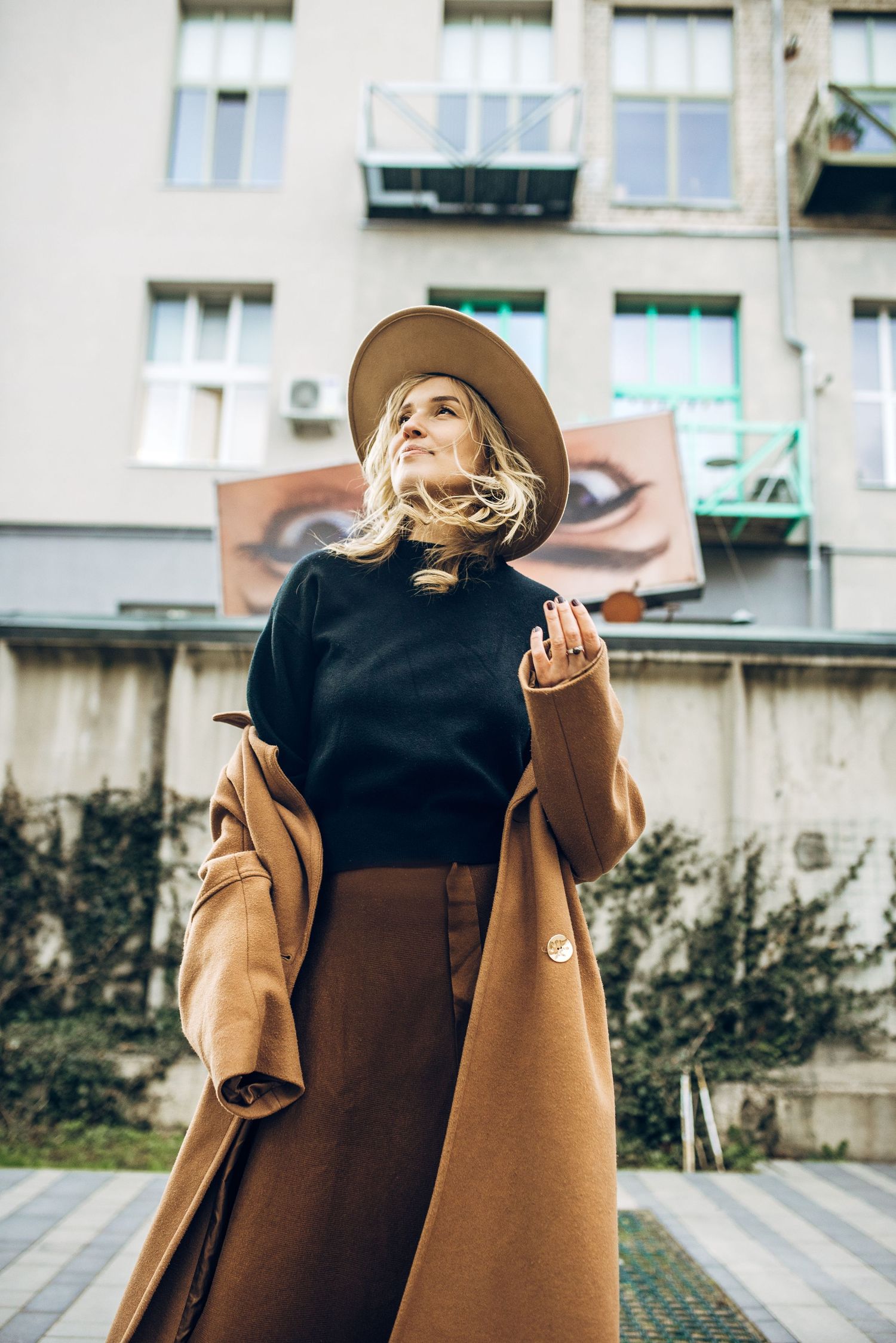 Fashion photography sequence showing a camel coat and hat ensemble against an urban backdrop.