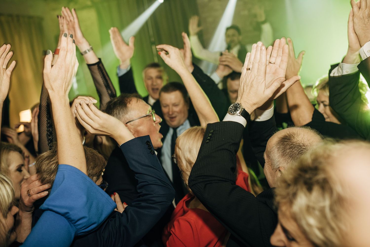 Crowd of people raising their hands during an energetic event with green lighting effects.