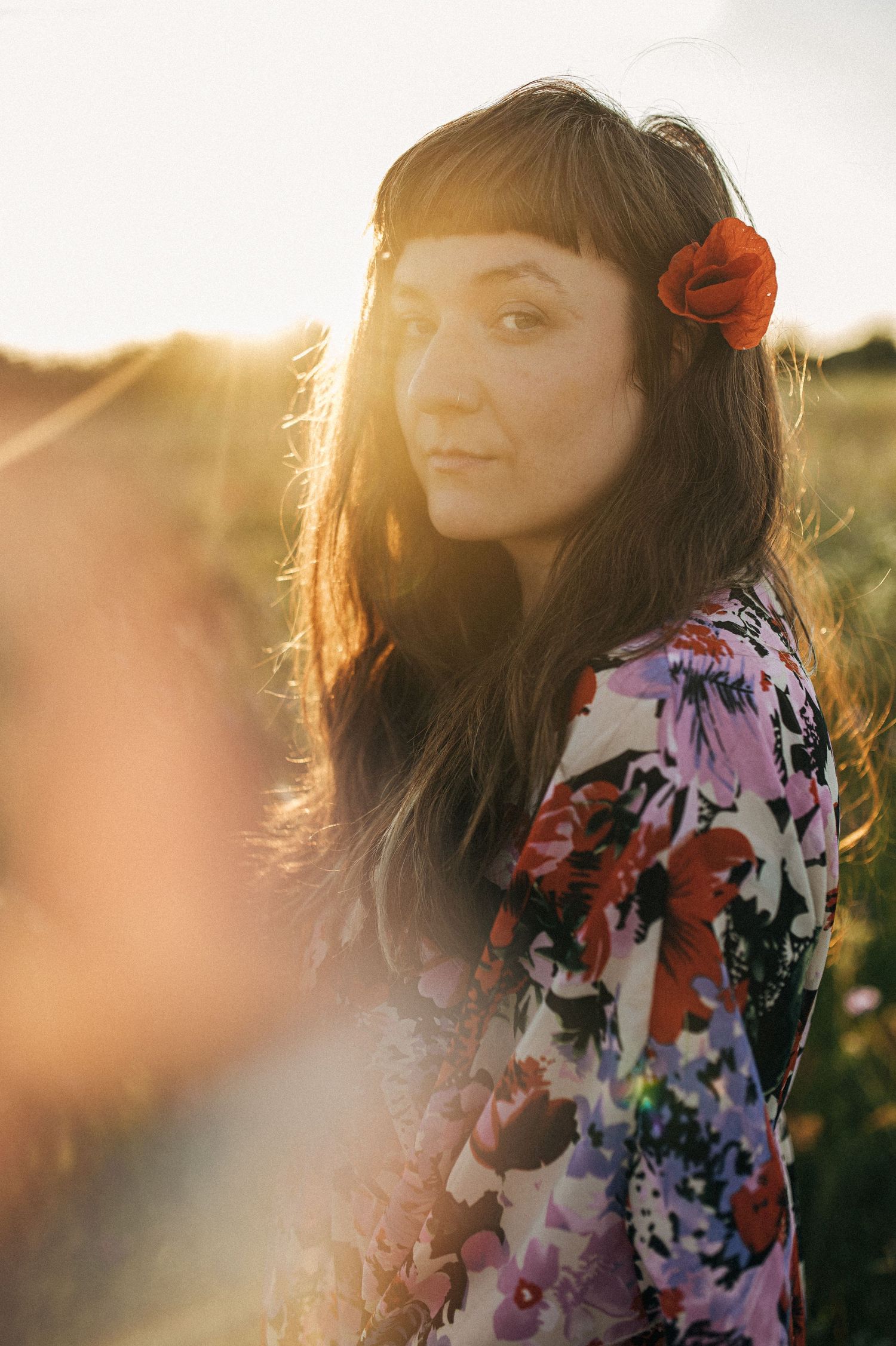 Dreamy sunset portrait with floral dress and red flower hair accessory creating romantic atmosphere.