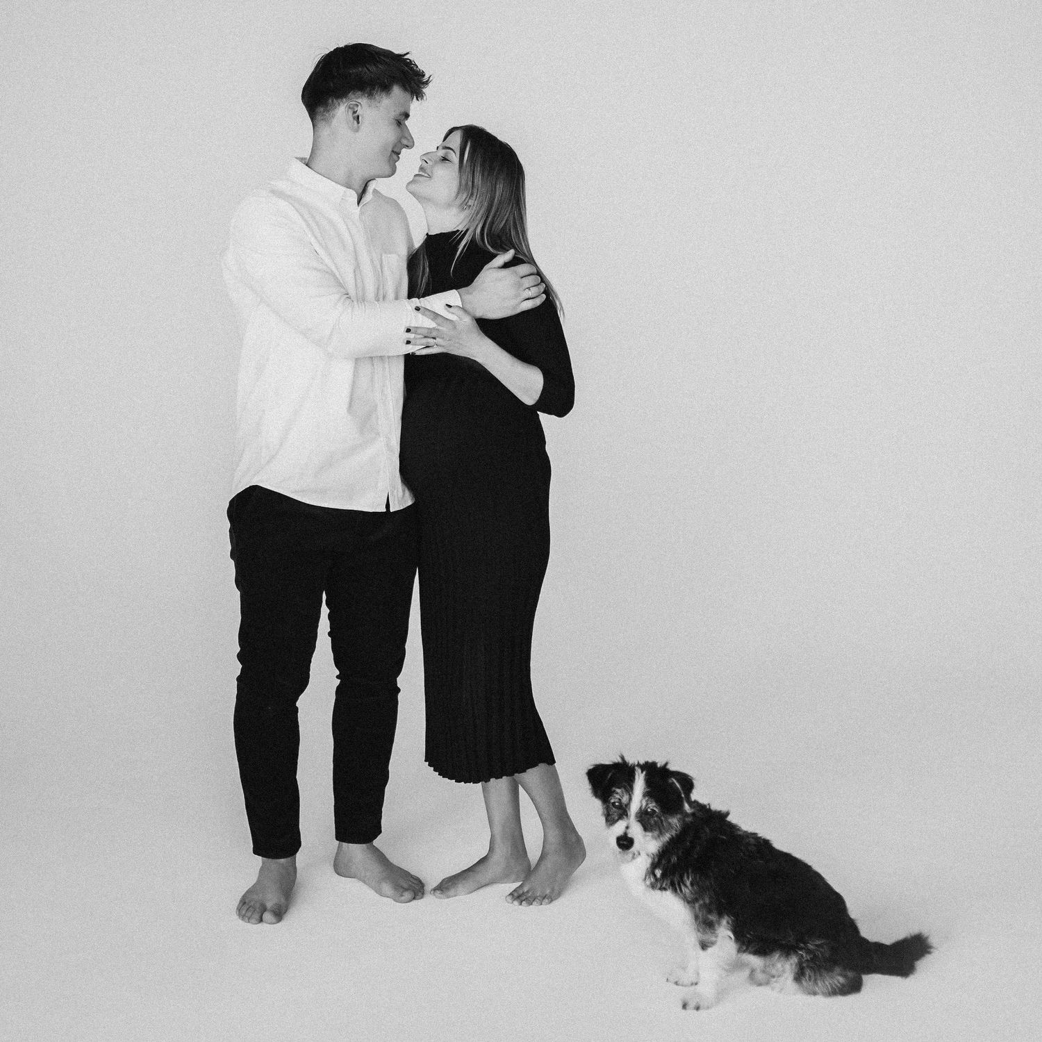 Black and white family photo session with pet dog against white background.