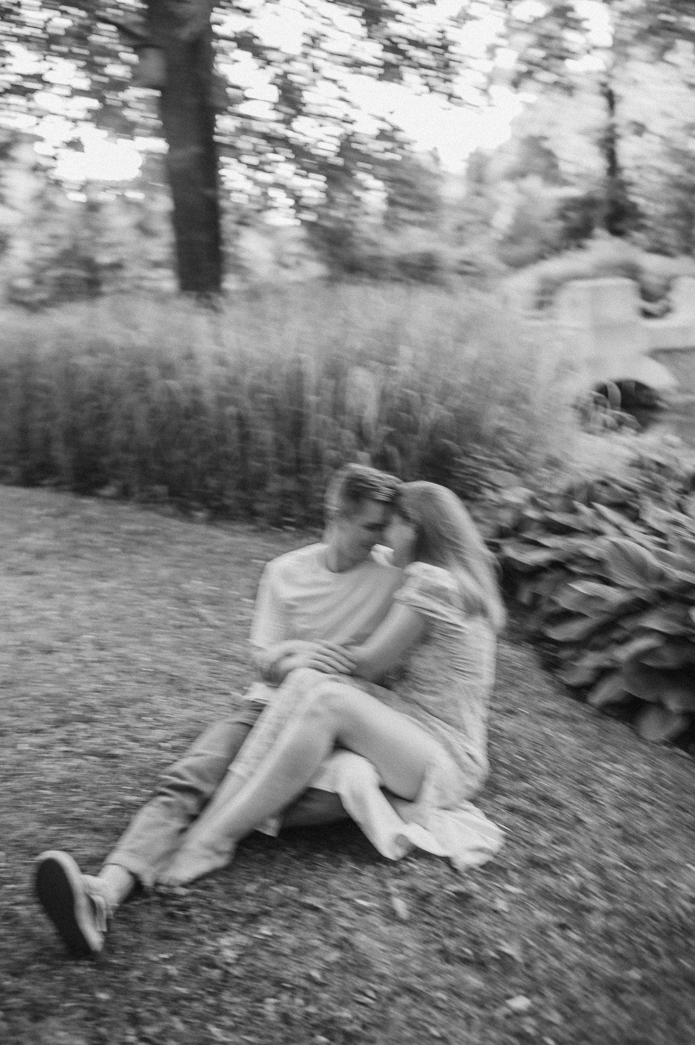 A black and white film photograph of a couple sharing an intimate moment on grass.