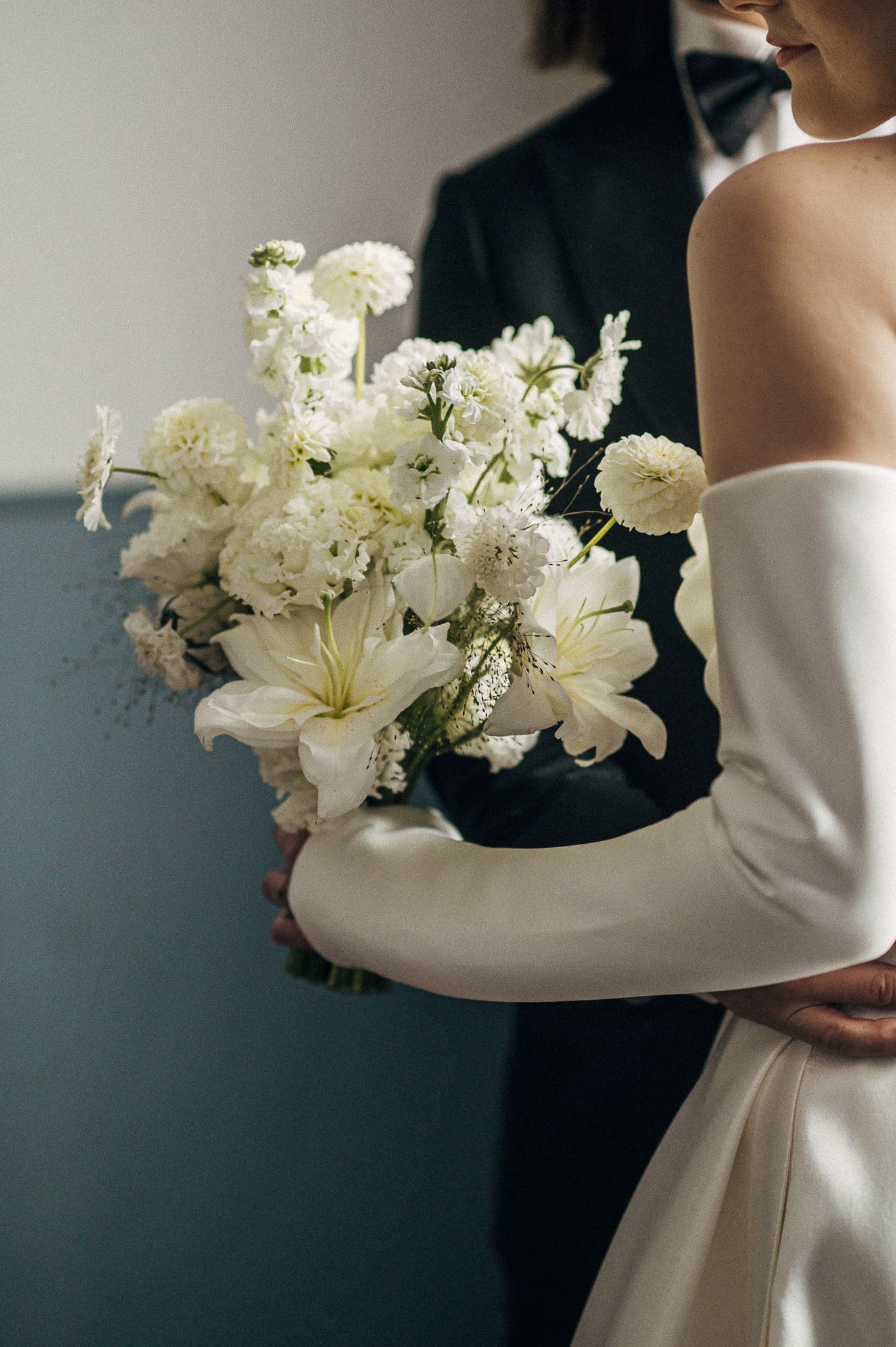 Elegant white floral arrangement with lilies held against a minimalist background.