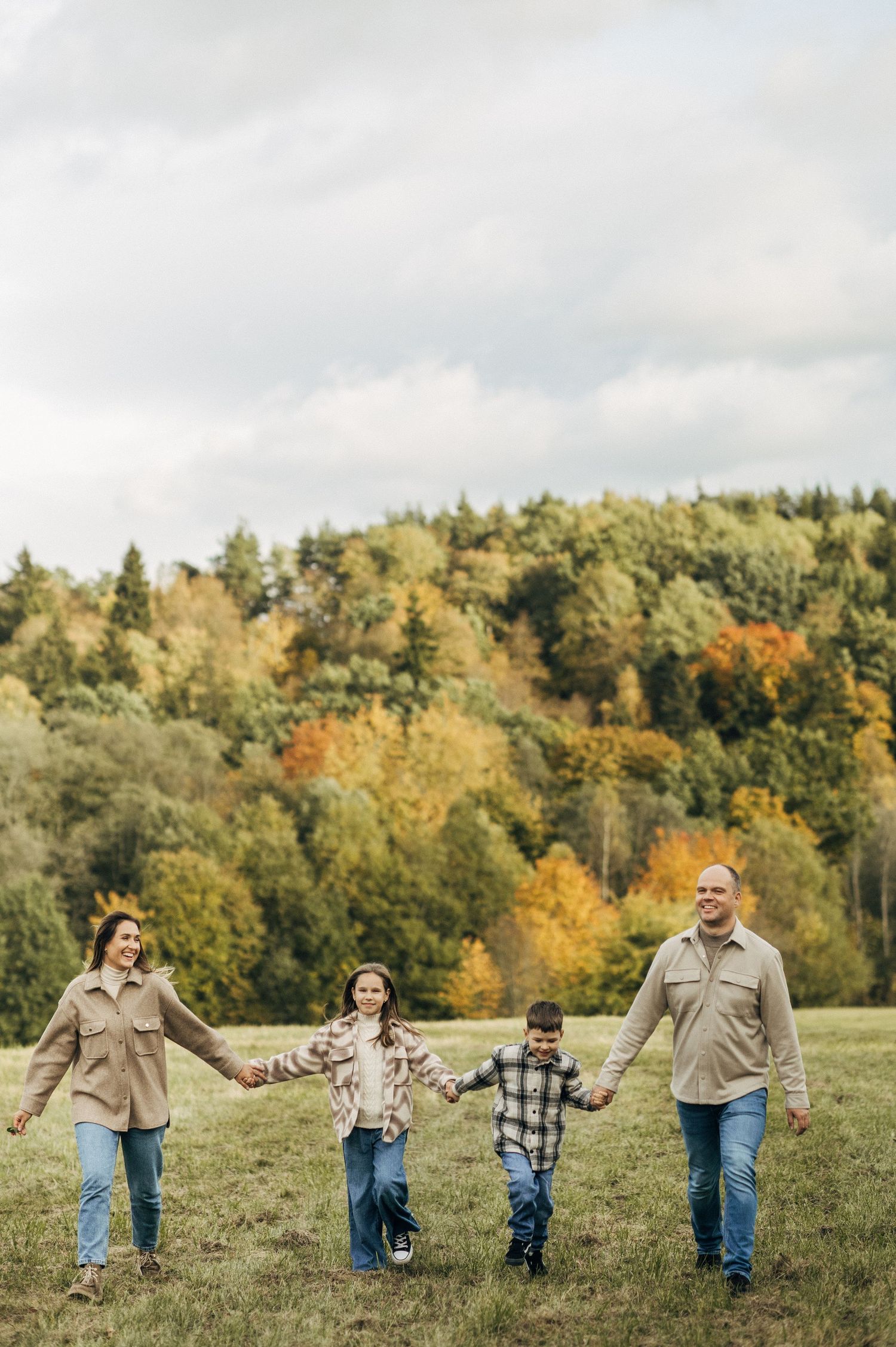 Family running and playing together in a grassy field with autumn trees in background.