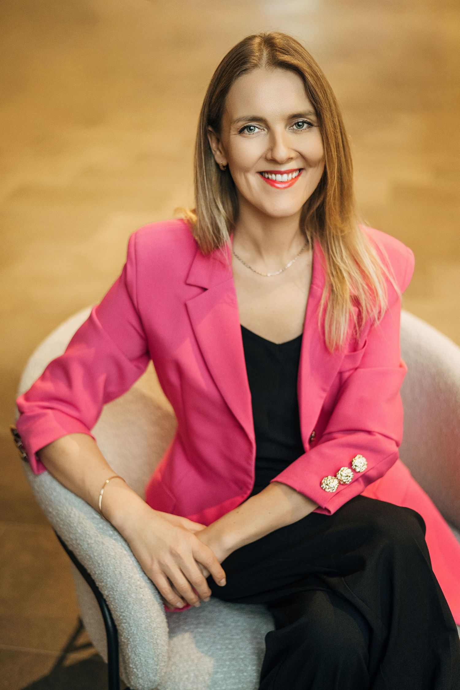Professional woman in bright pink blazer and black dress sits confidently in business portrait series.