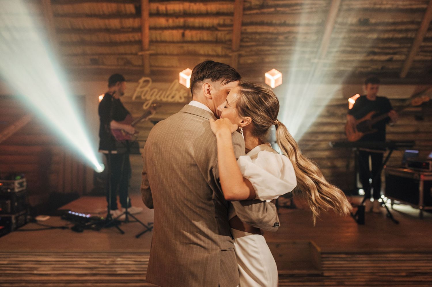 Dancing couples illuminated by spotlights in a rustic wooden barn venue.