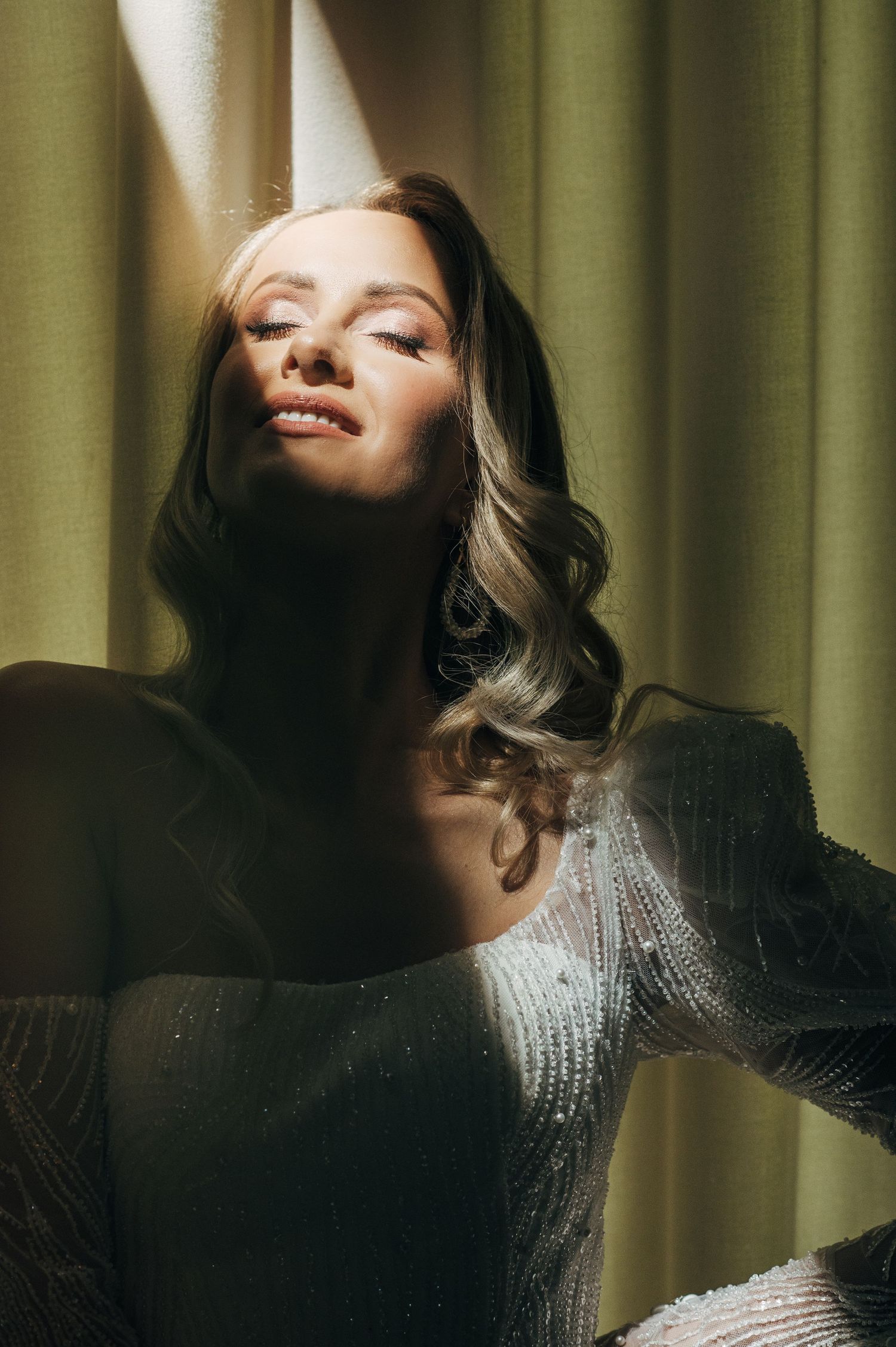 Artistic portrait of bride in lace dress with dramatic lighting and green curtain backdrop.