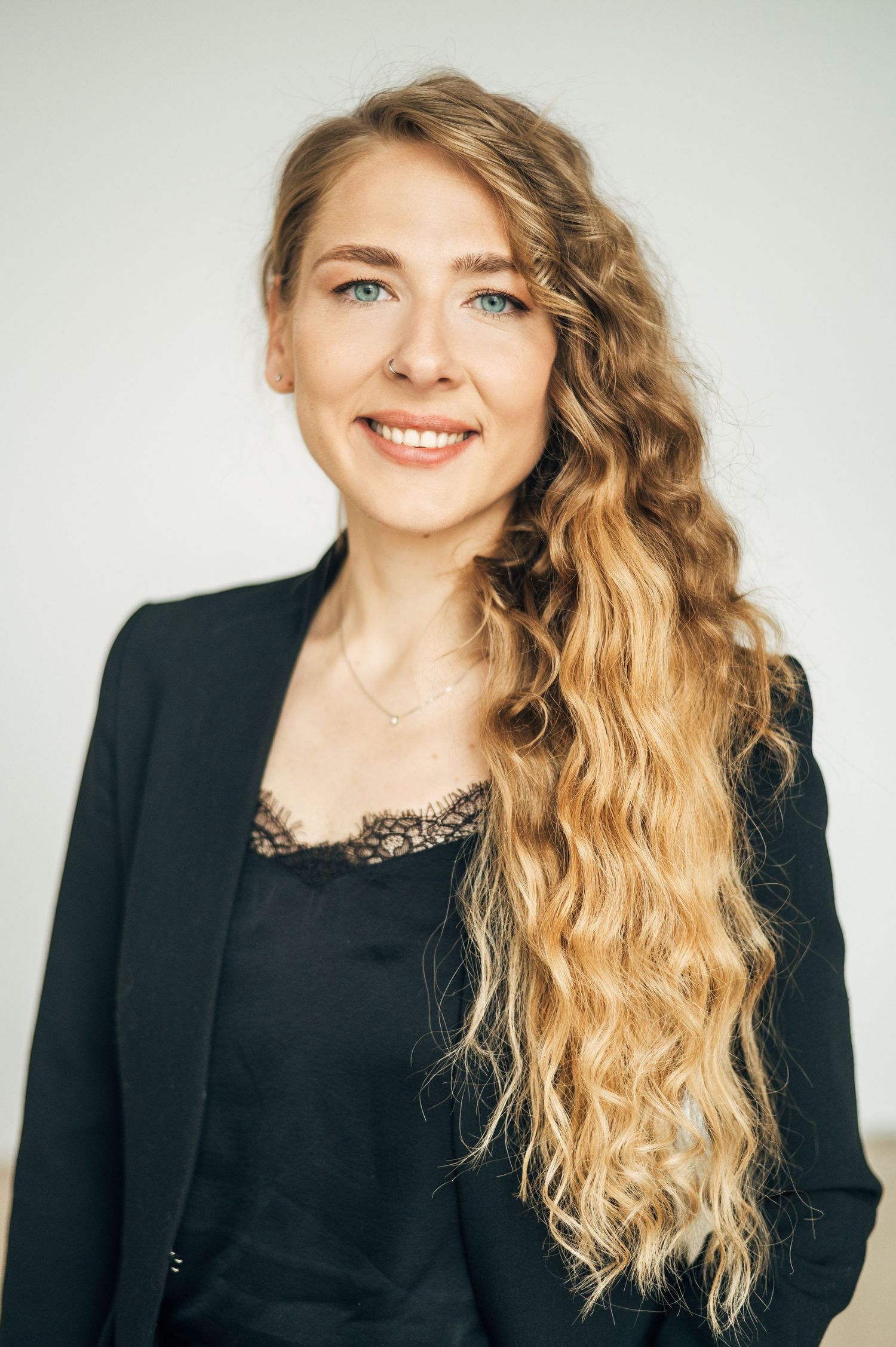 Professional portraits with wavy blonde hair wearing black blazer against white backdrop.