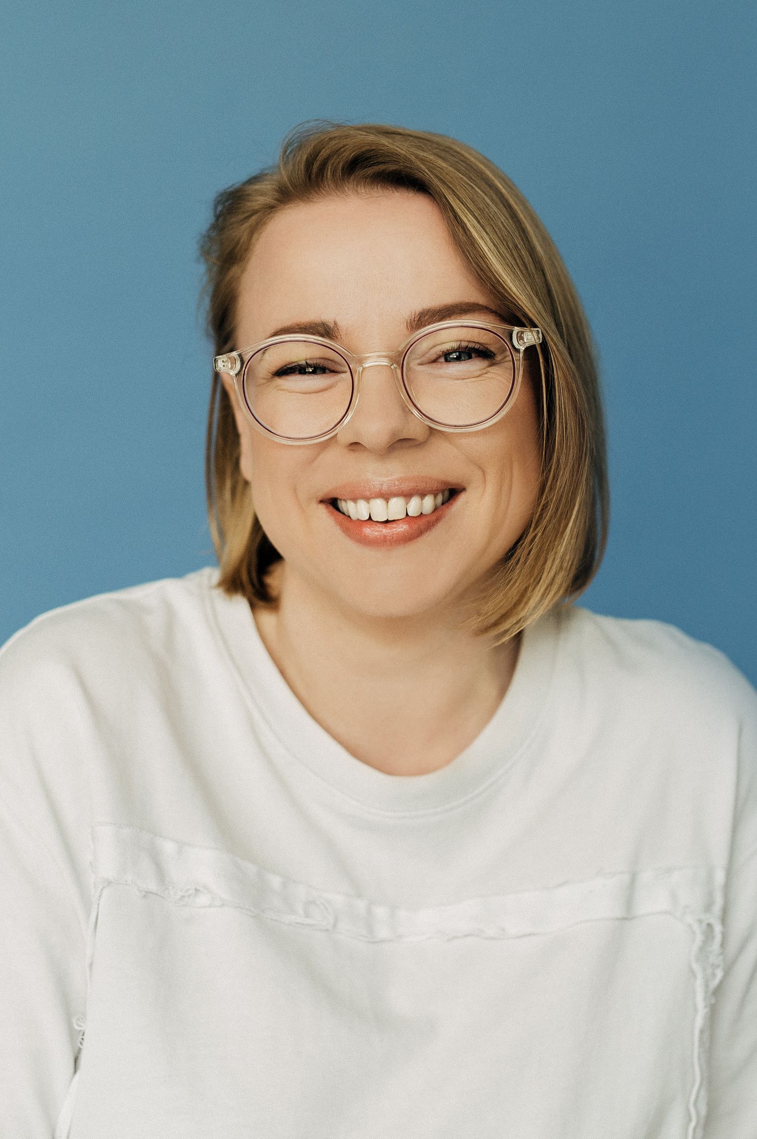 Portrait of someone wearing glasses and white shirt against blue background with joyful expression.