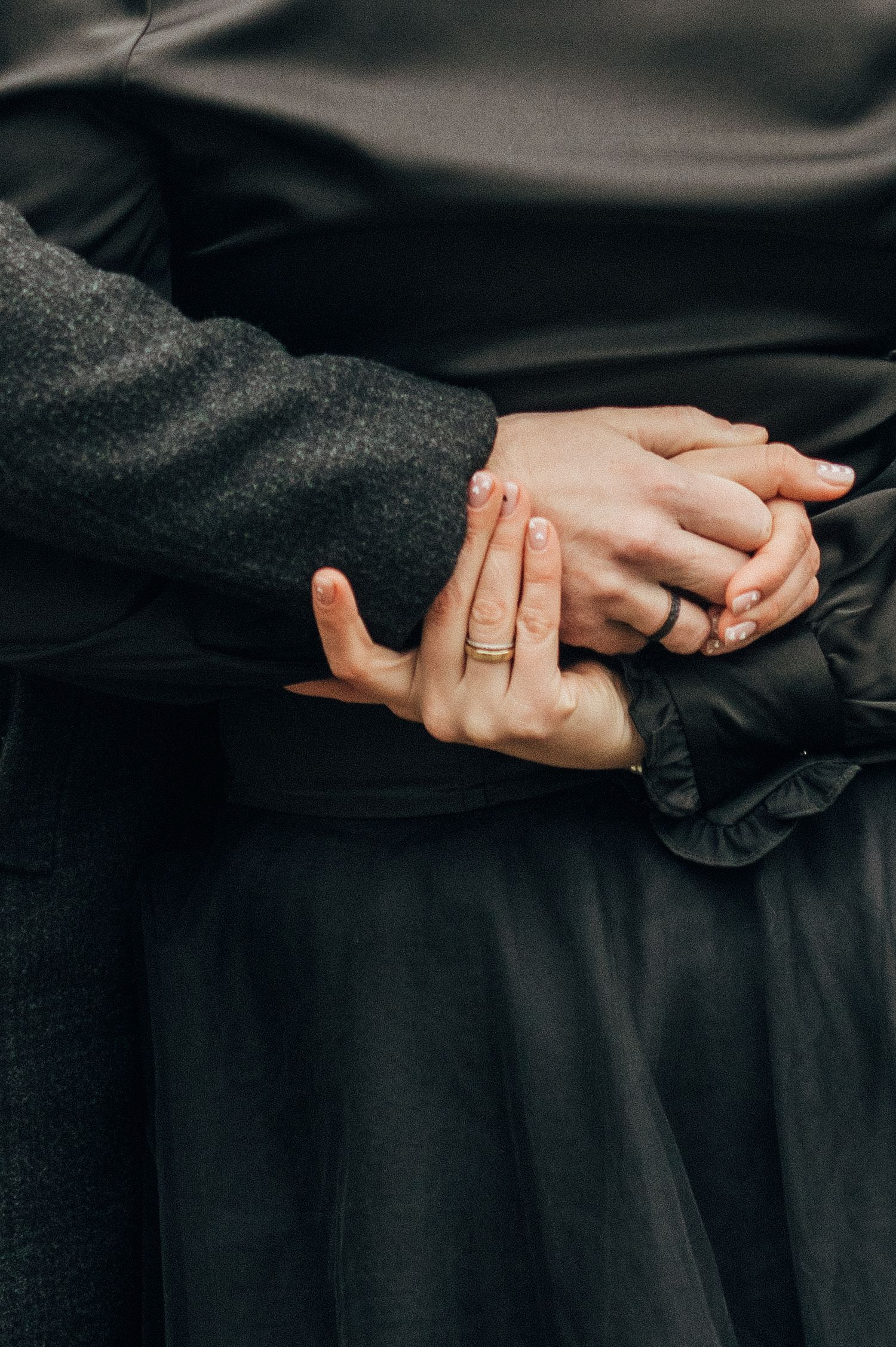 Close-up of hands wearing rings touching and holding each other against black fabric.