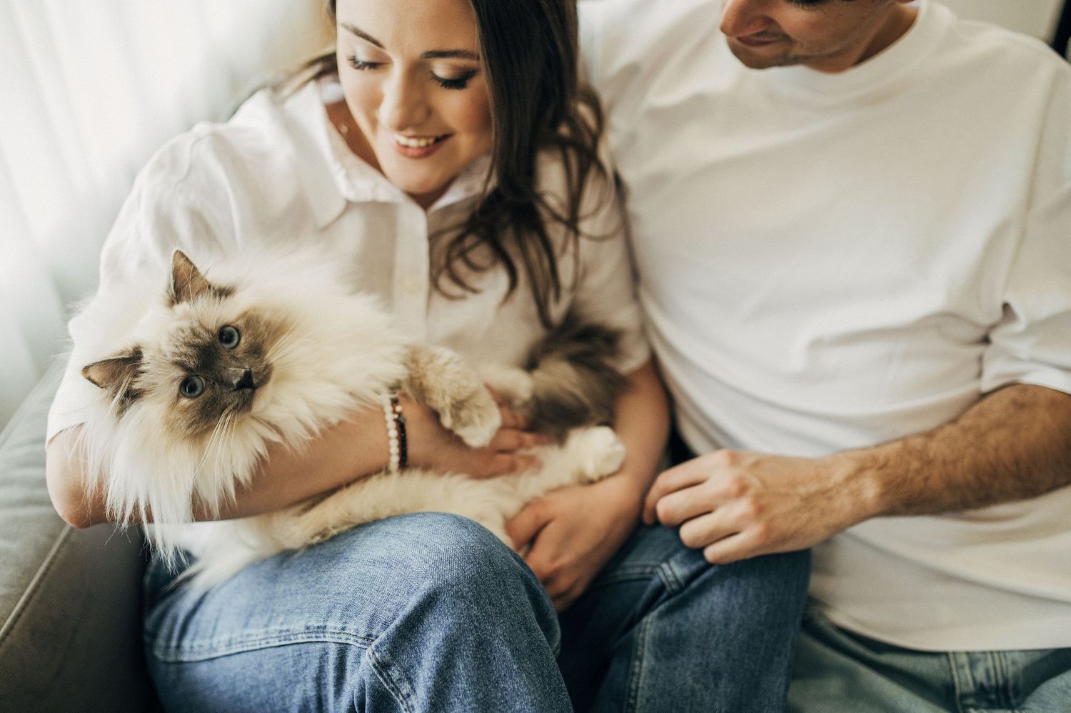 Relaxed couple lounging on couch with fluffy cat in casual home setting.