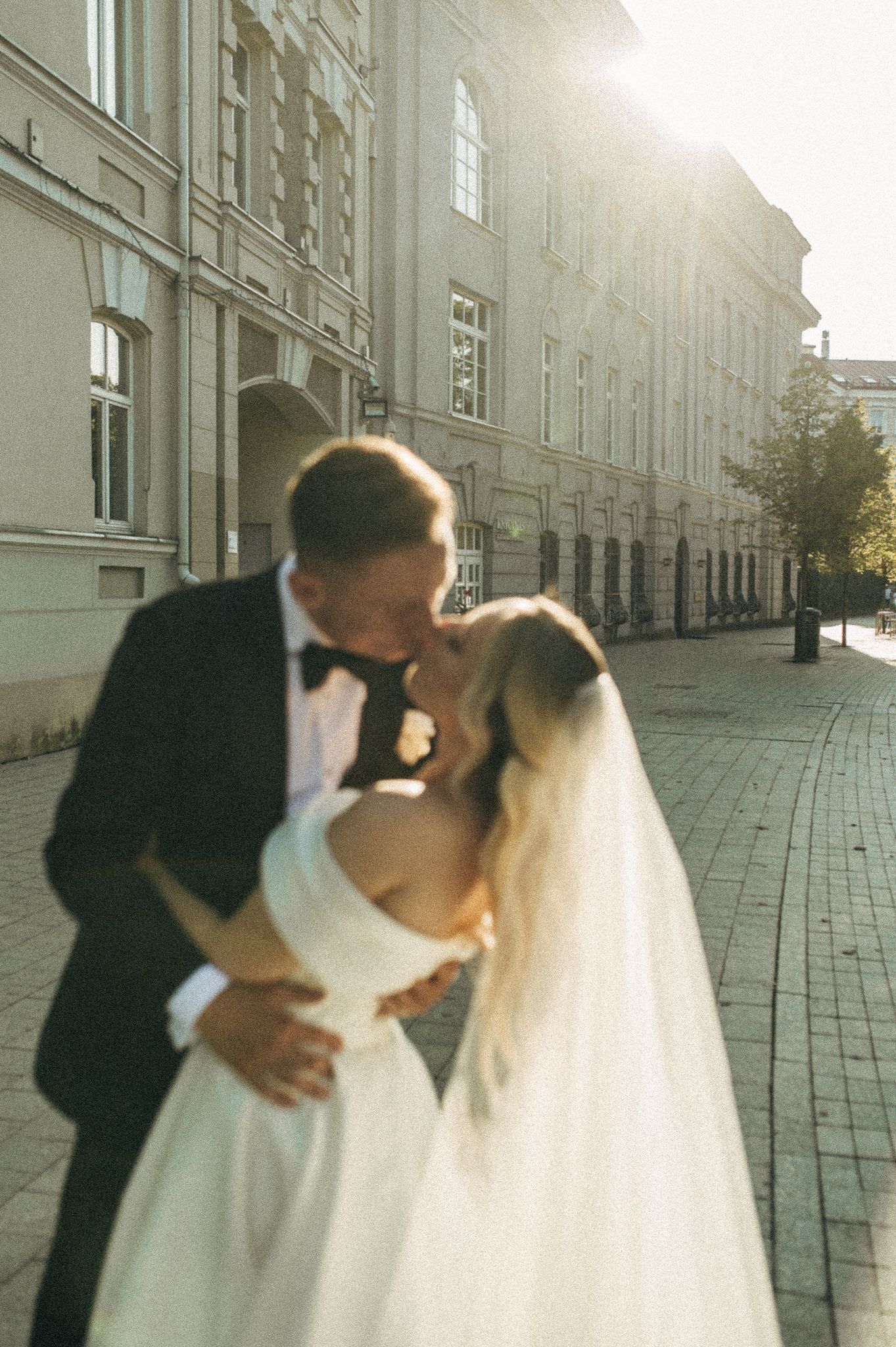 A bride and groom share romantic kisses in a series of photos against a sunlit stone building exterior.