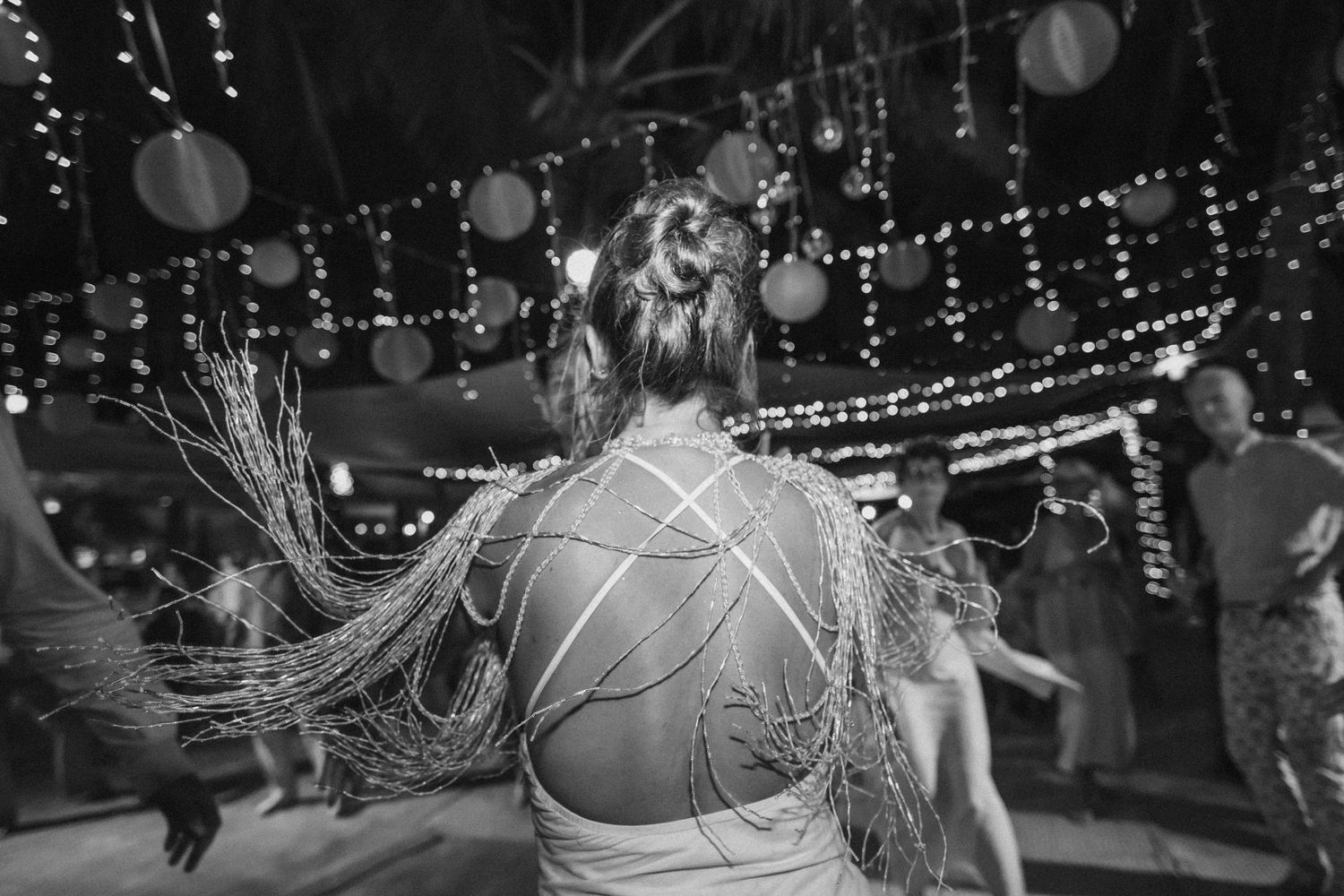 A black and white photo of a dance celebration with string lights and lanterns decorating the venue.