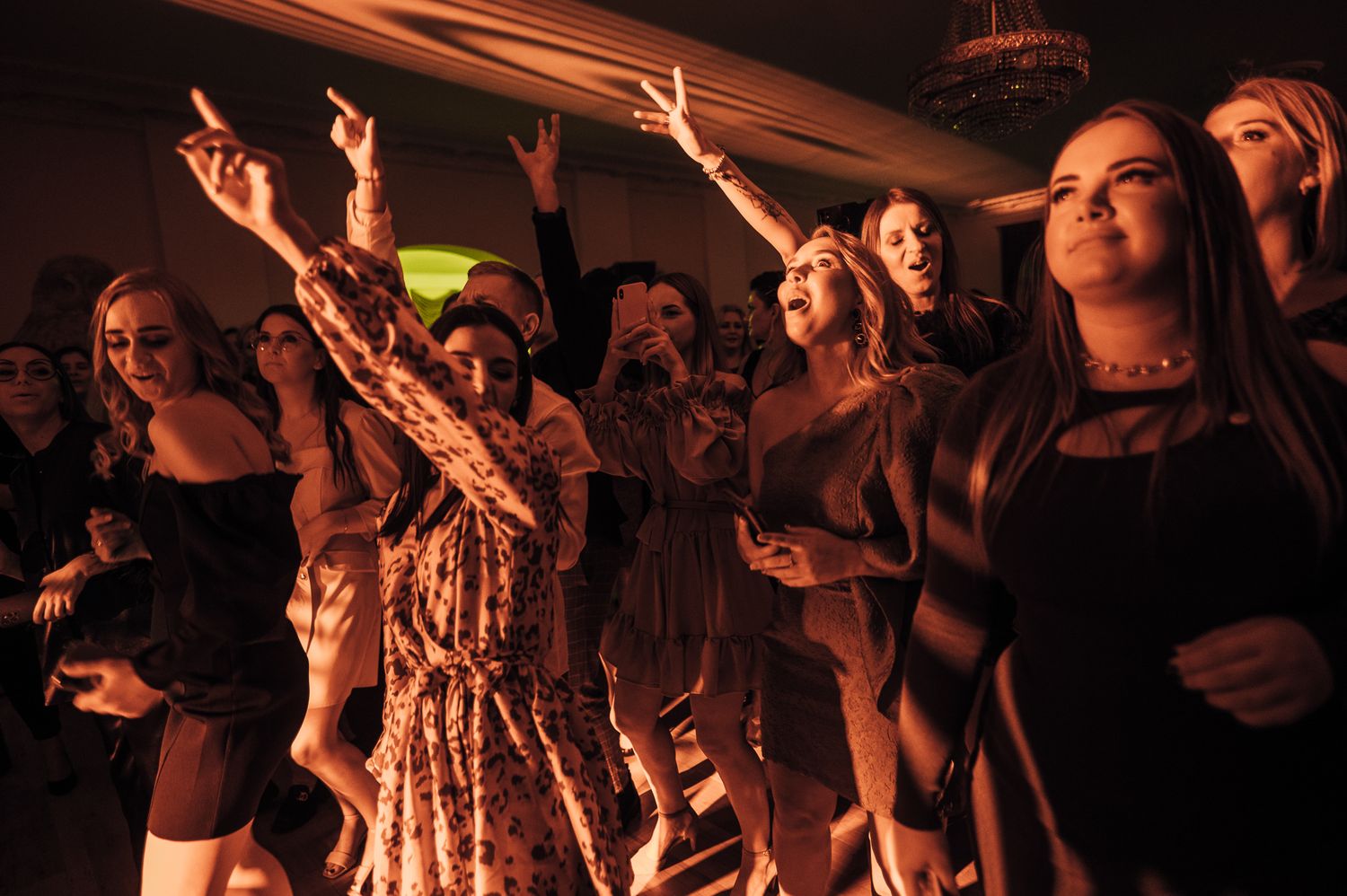 Energetic crowd dancing and celebrating at a dimly lit party with red lighting.
