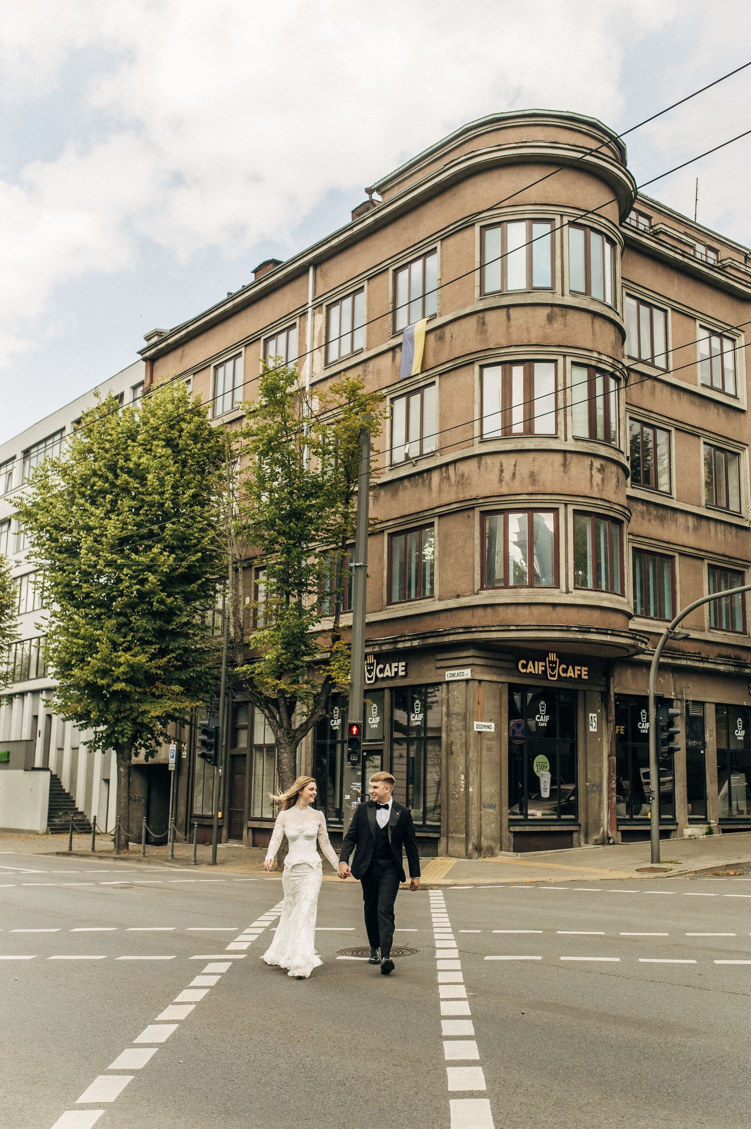 Elegant couple walking across urban crosswalk near historic Art Deco style building on corner street.