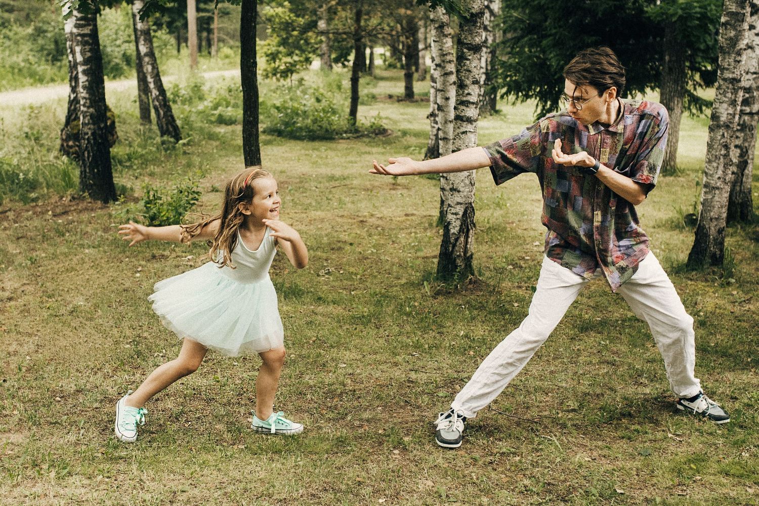 Father and daughter playing and dancing together in a green forest park outdoors.