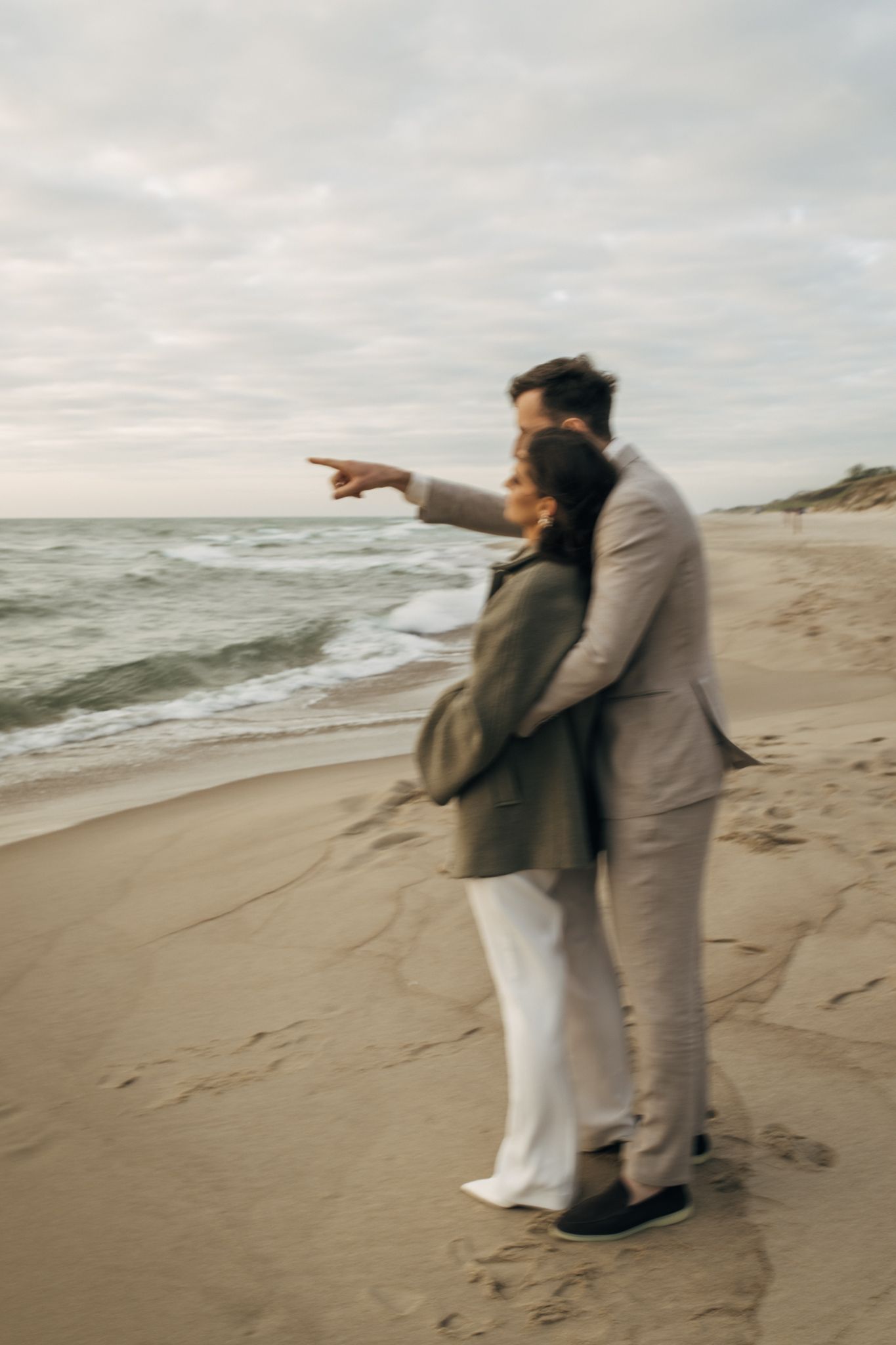 Couple in wedding attire shares playful moment on windy beach.
