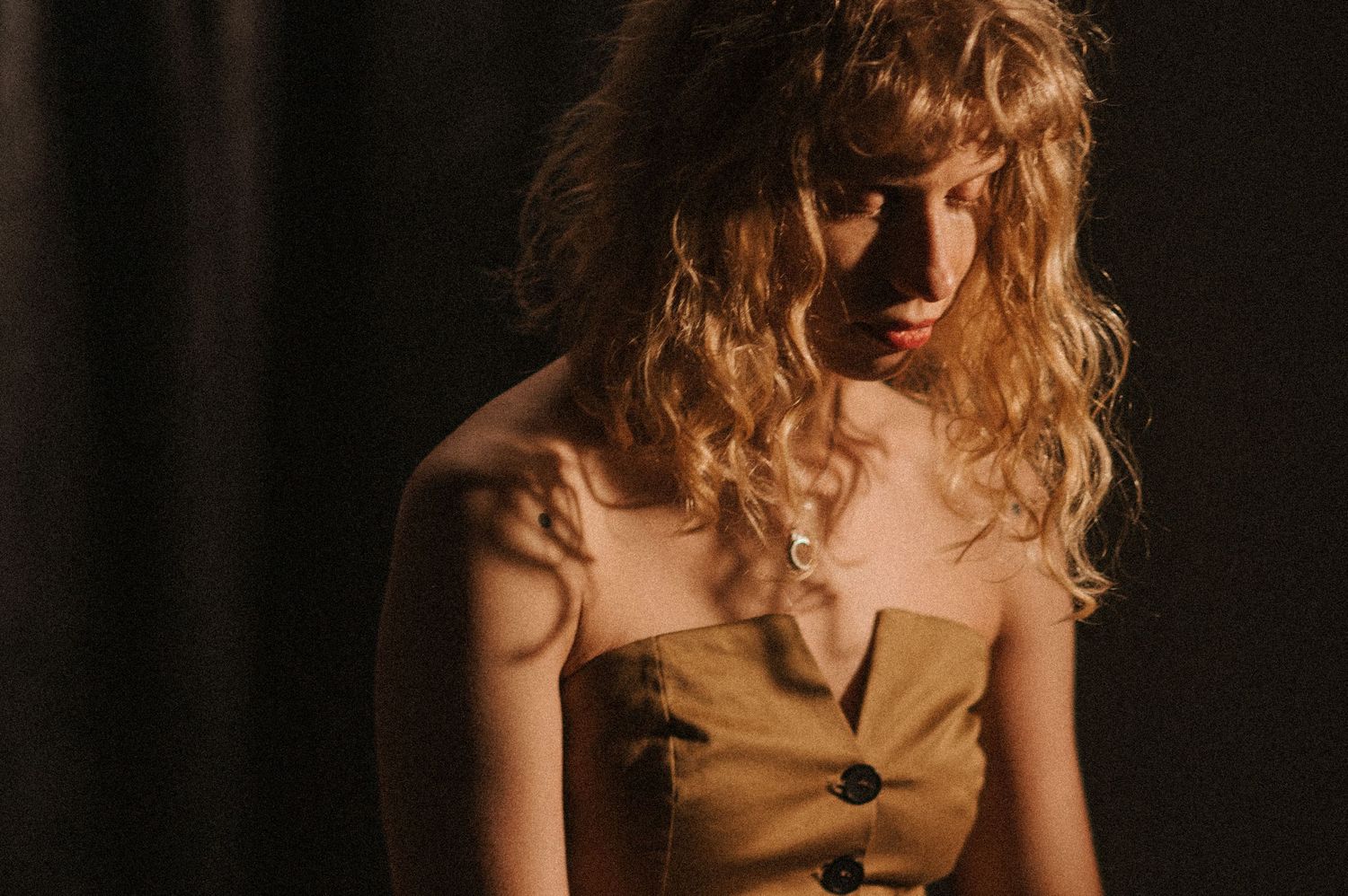 Artistic portrait of model in tan dress with curly hair in moody lighting.