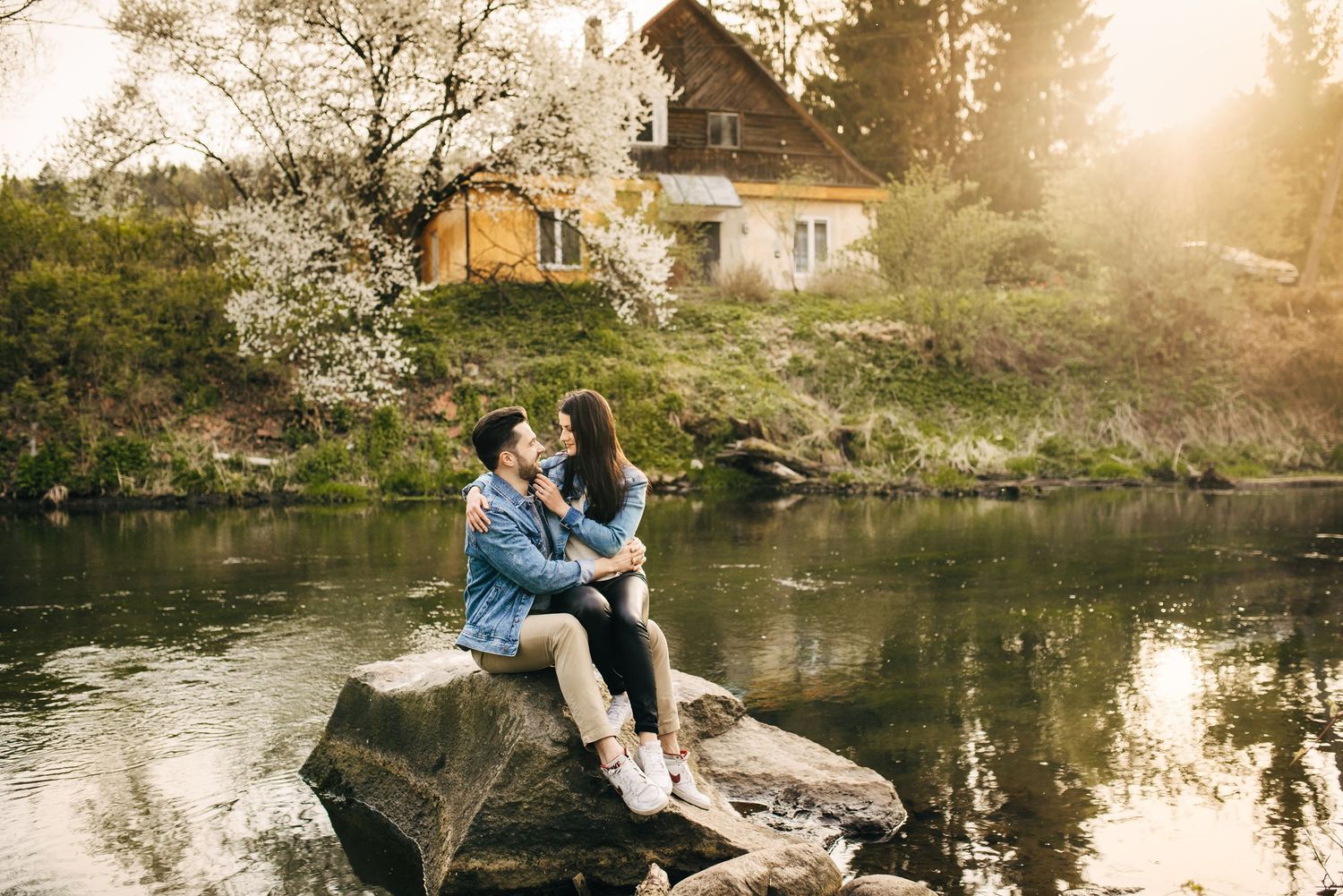 Romantic couple poses together by a serene pond in a natural setting during golden hour sunset.