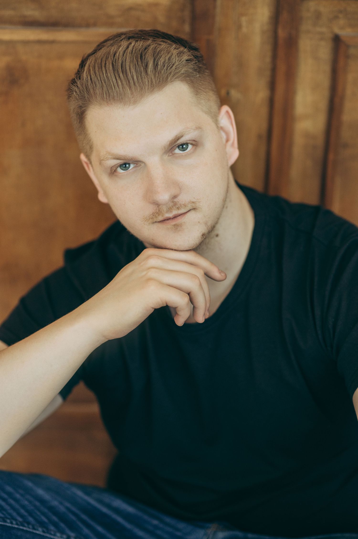 Moody portrait series of someone in black attire against wooden wall background.