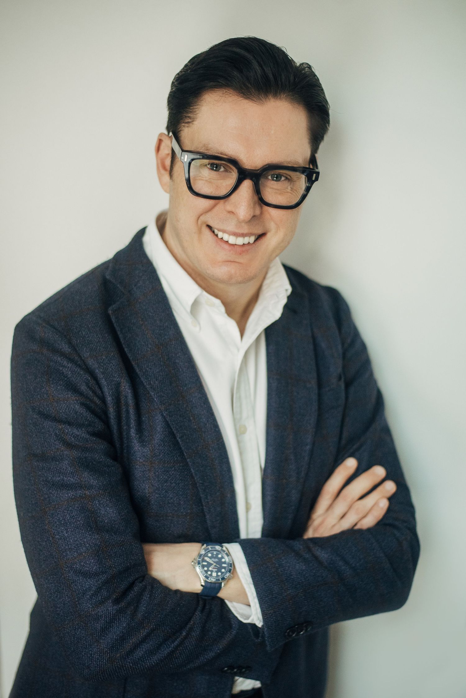 Business professional in dark suit and white shirt poses against light background with confident smile.