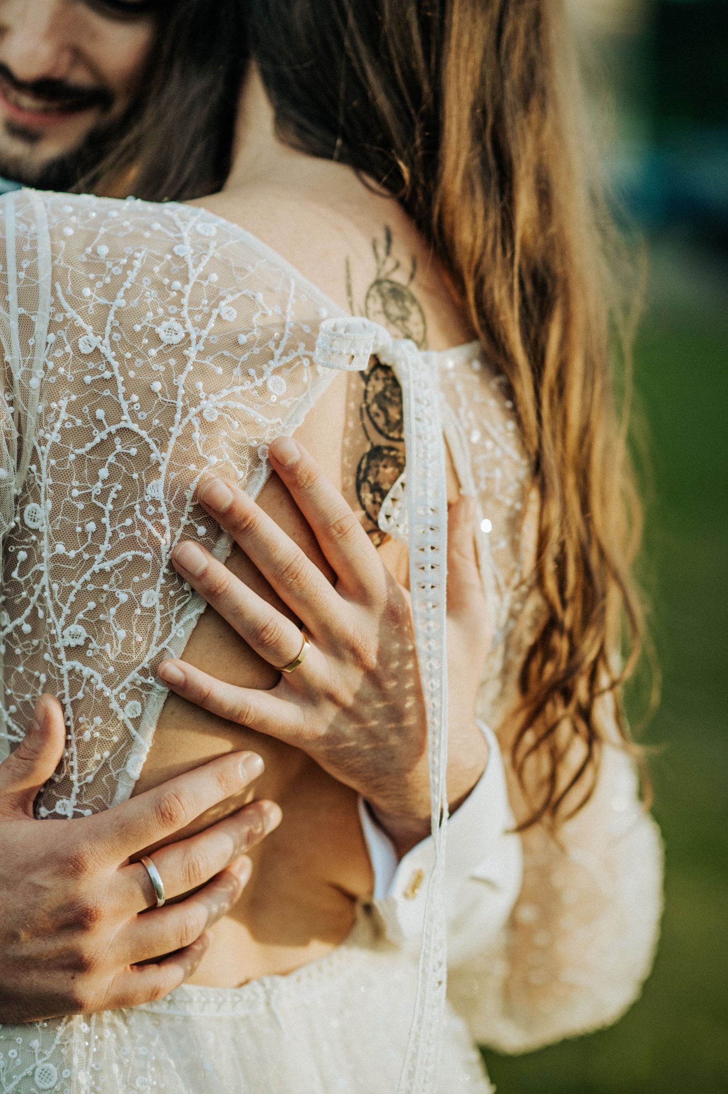 Close-up detail of delicate lace wedding dress with hands showing wedding rings.
