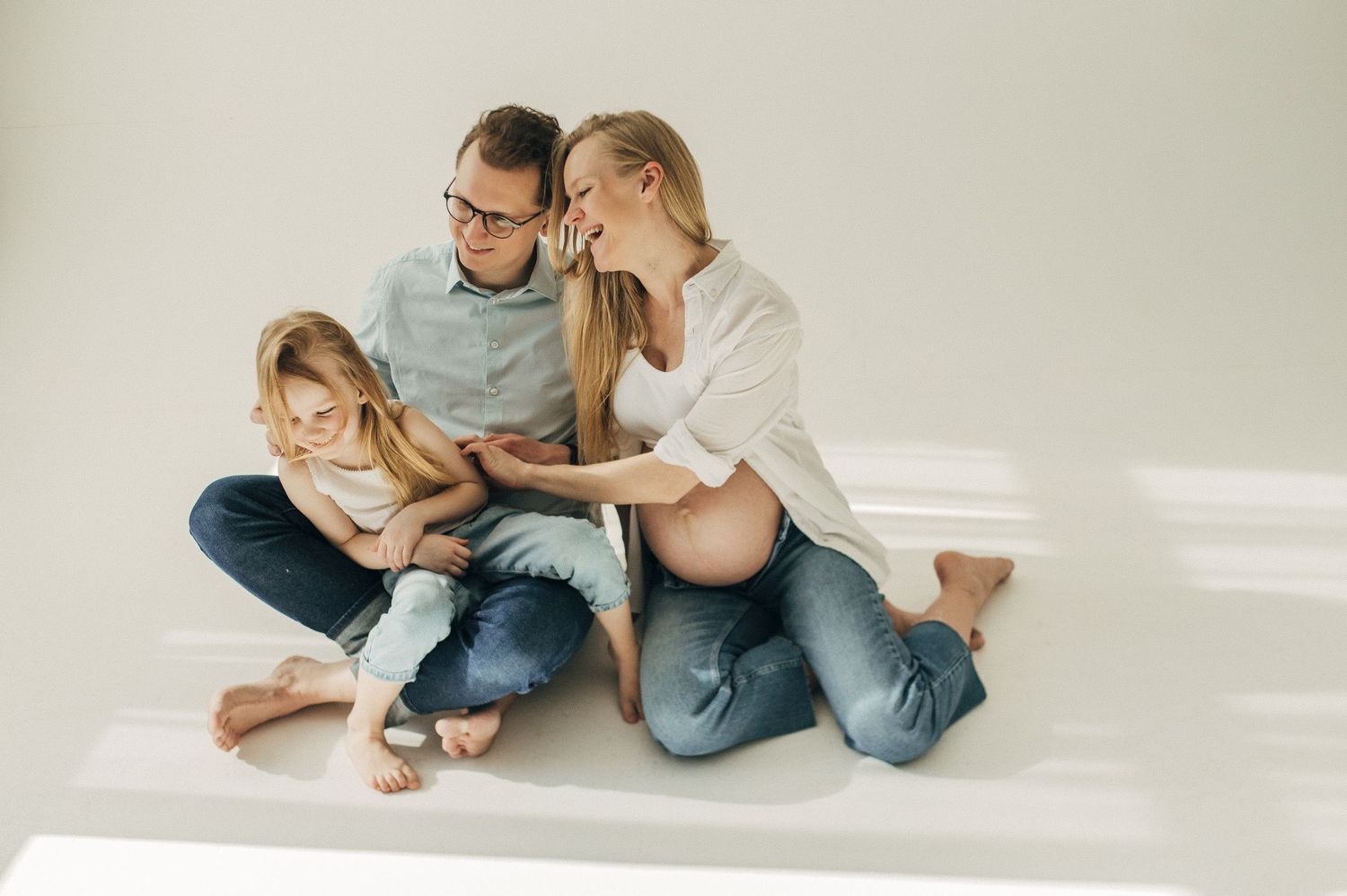 Family photos captured in minimalist white room showing tender moments together.