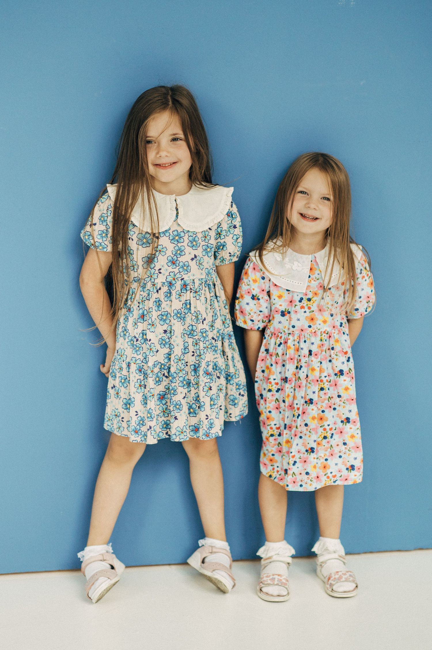 Playful studio portraits with matching floral dresses against blue background.