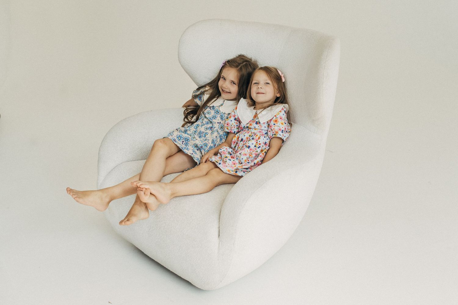 Two children lounging together on white modern chair during photo session.