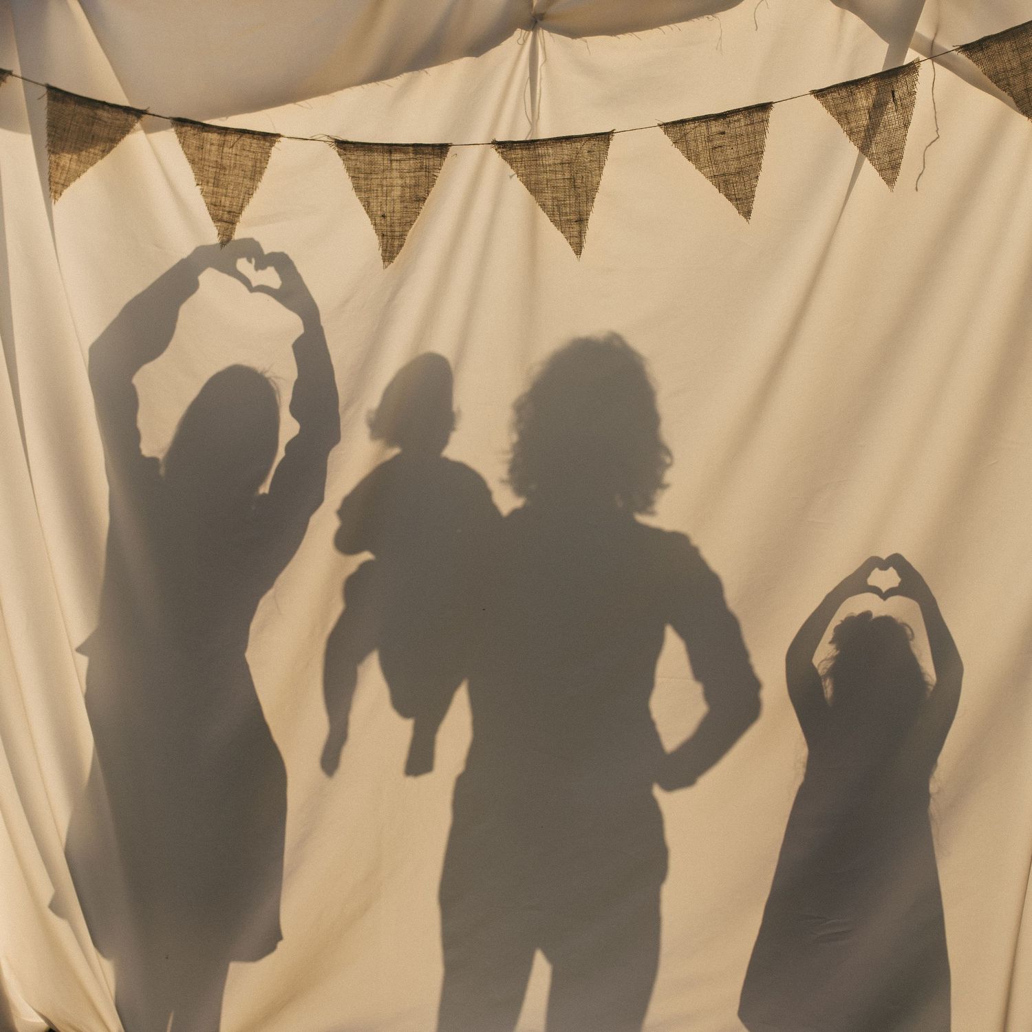 Silhouettes of a family with baby making heart shapes with hands against a cream backdrop.