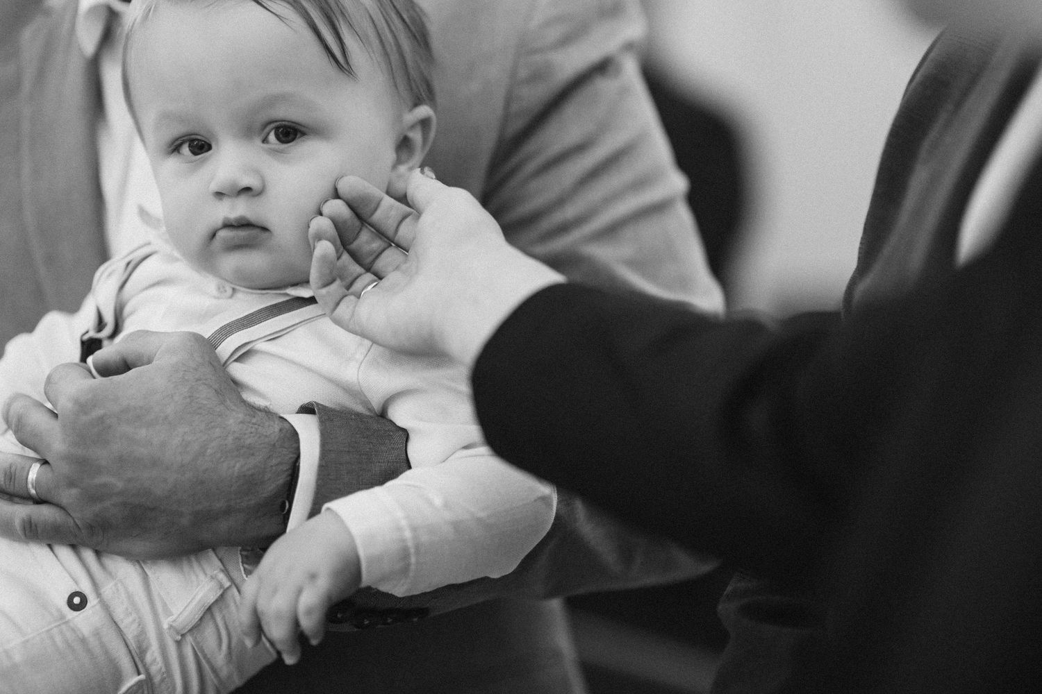 Black and white tender moment of adults gently cradling and touching an infant's face.